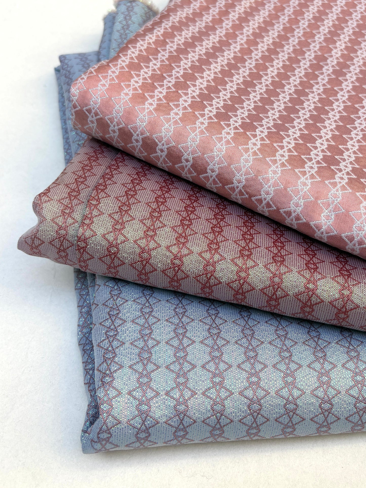 Stack of patterned silk fabric, folded, in shades of blue, pink, and gray.