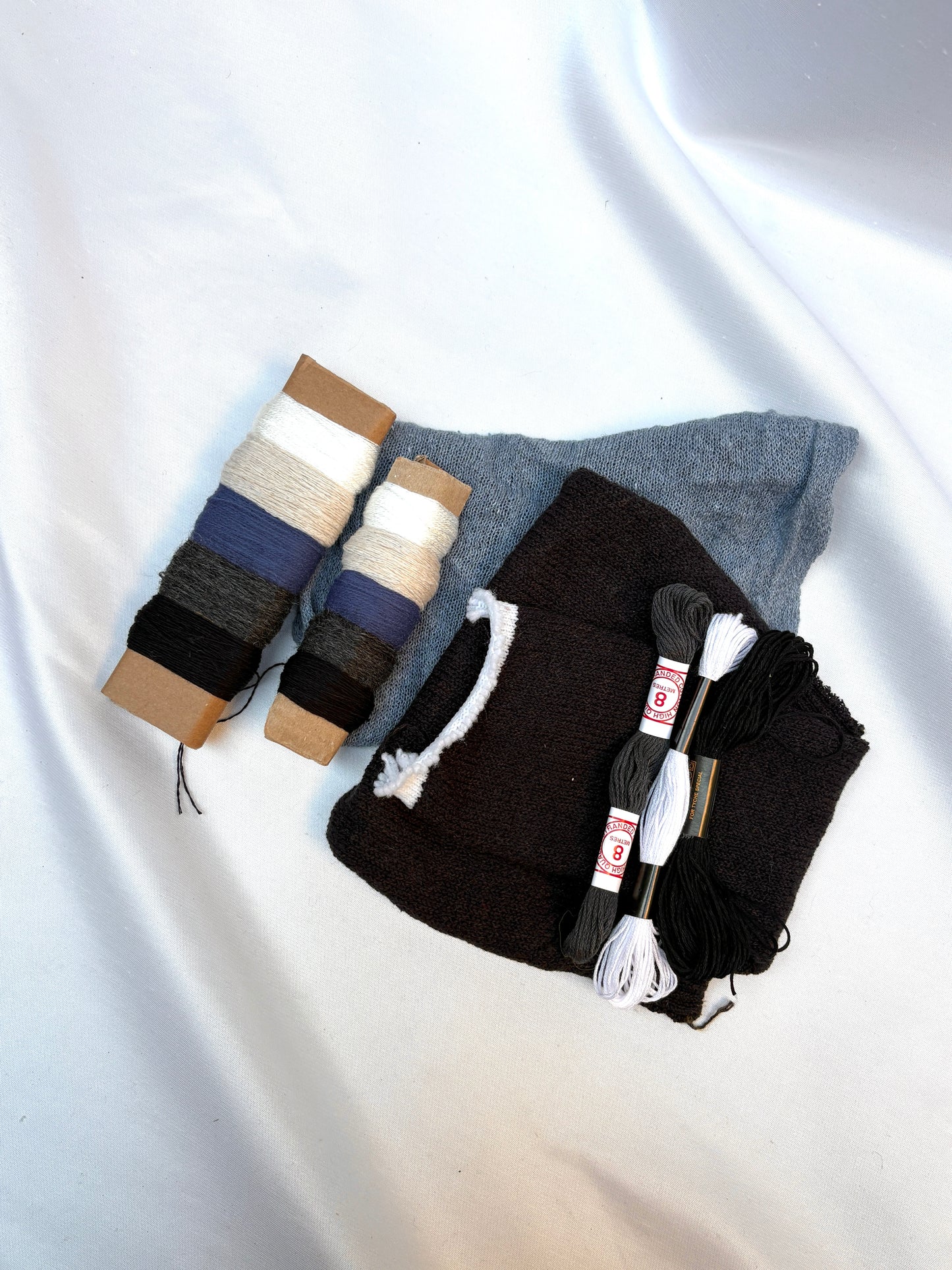 Sewing materials arranged on white fabric with thread, cloth and embroidery floss.