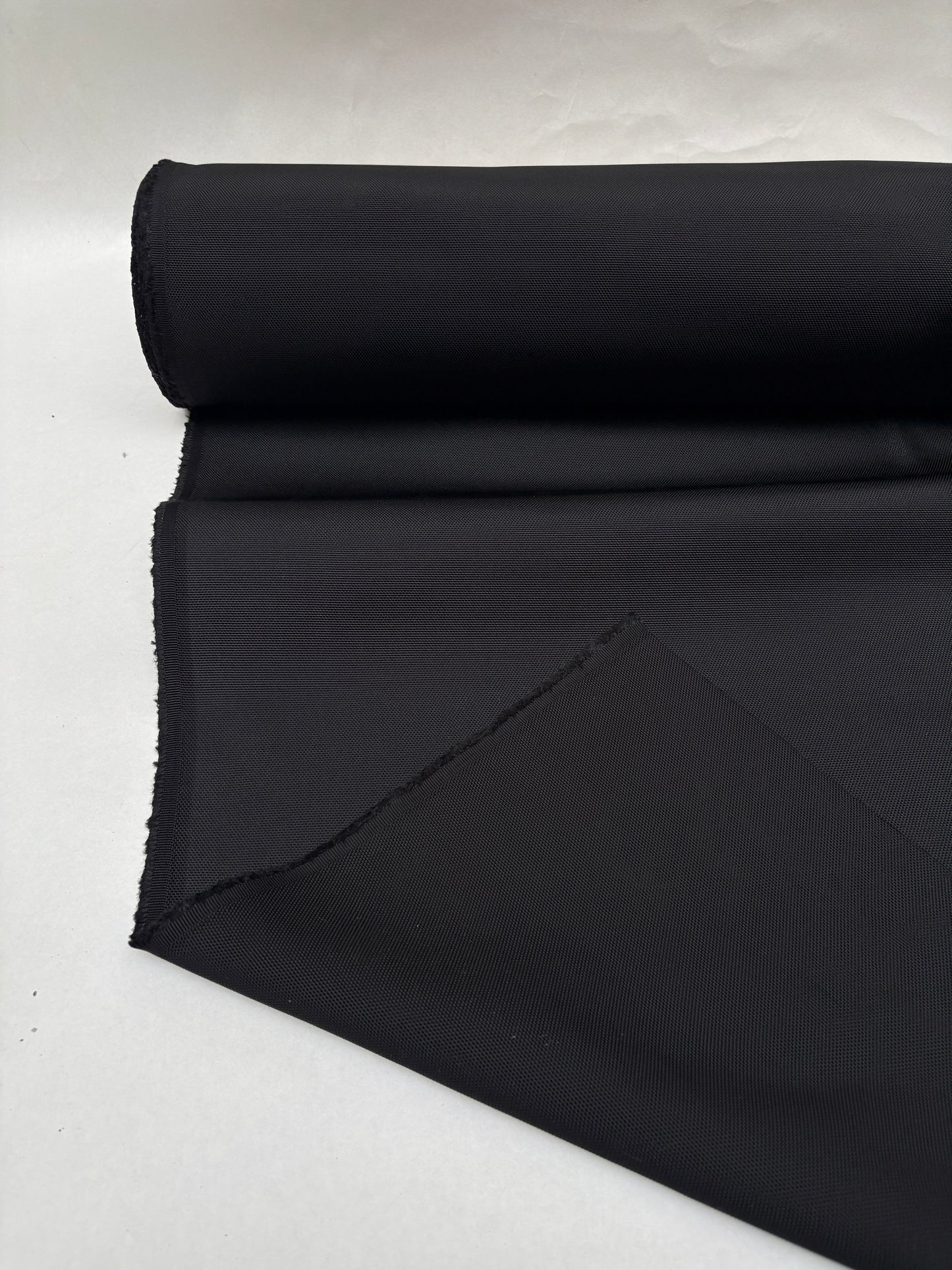 Dark textured fabric is shown hanging from a roll with a fold