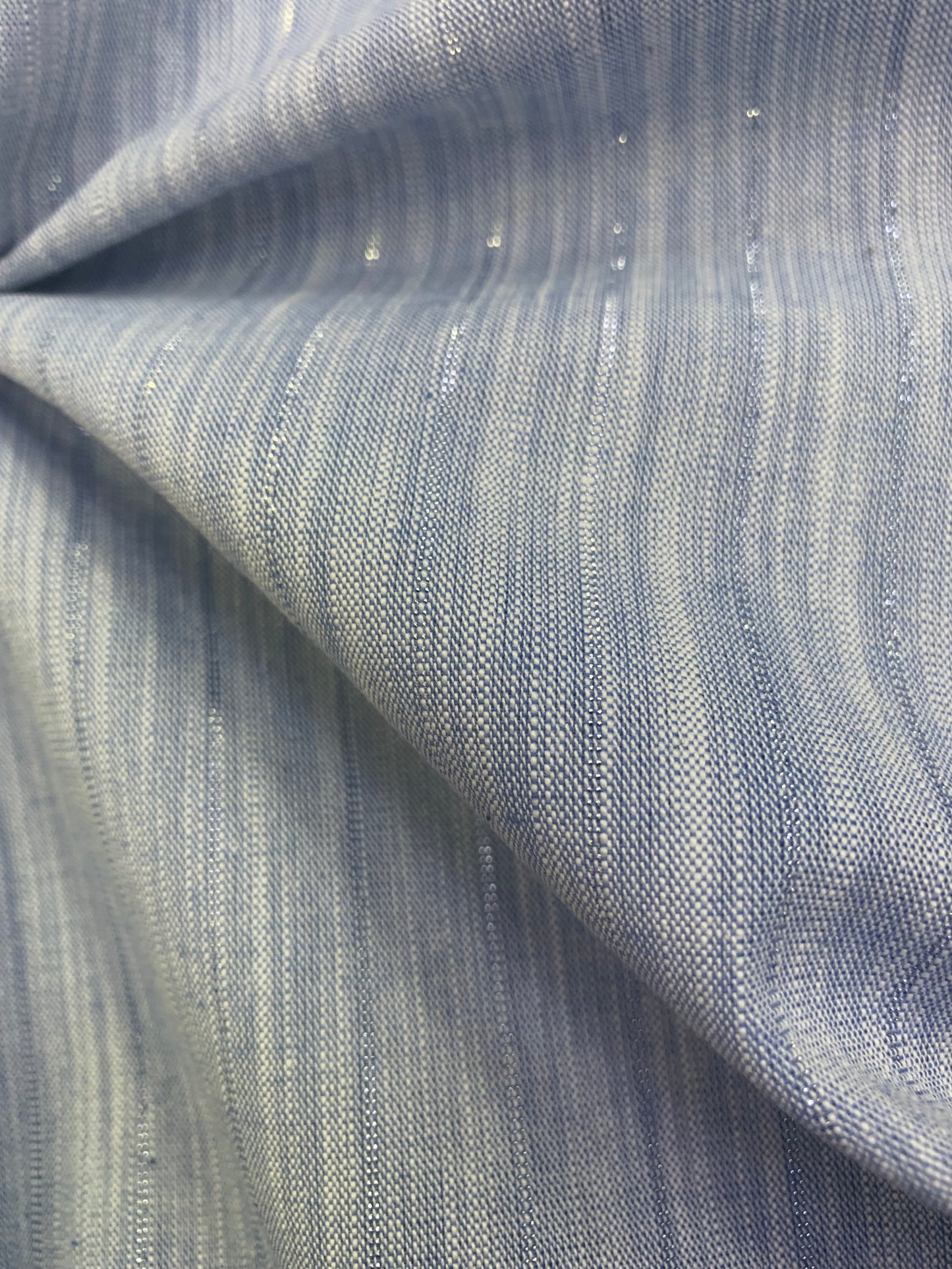 Textured close-up of pale blue stripe lurex chambray deadstock fabric.