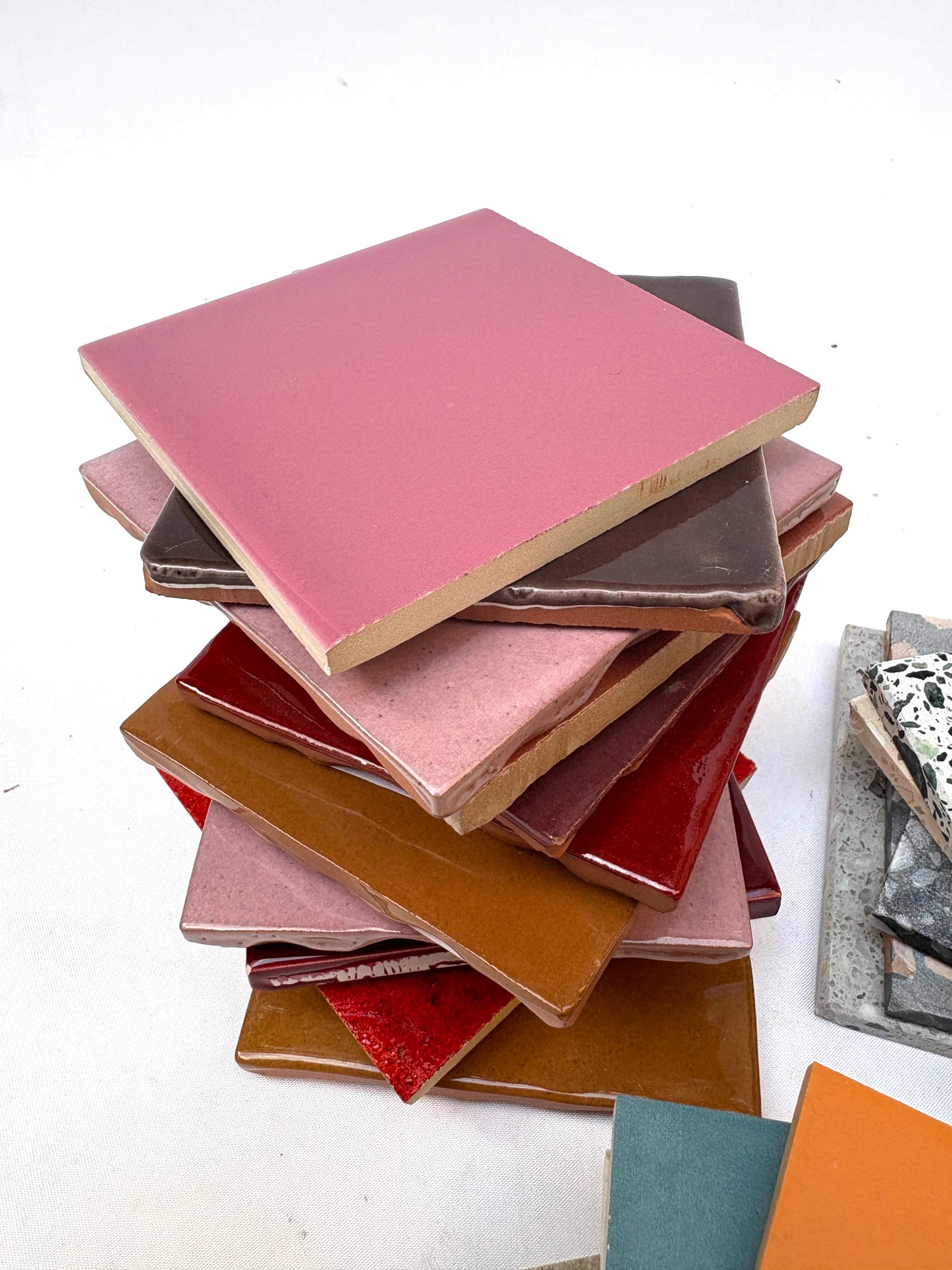 Pink, orange, and patterned sample tiles are stacked together on white