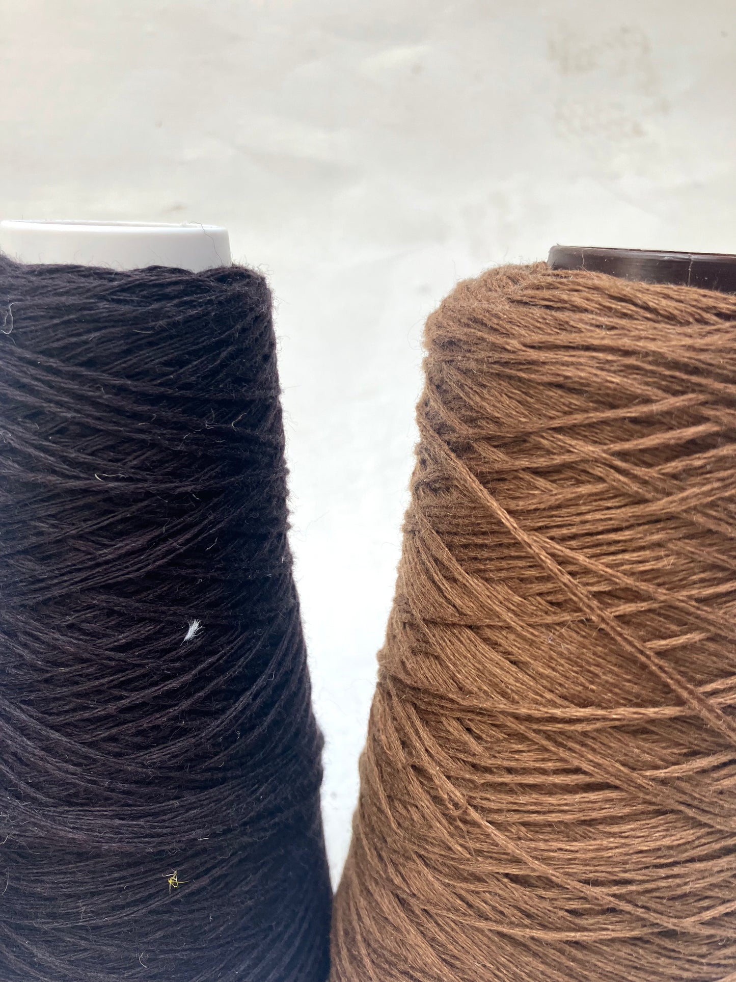 Close-up of yarn cones in dark neutral shades on a white background.