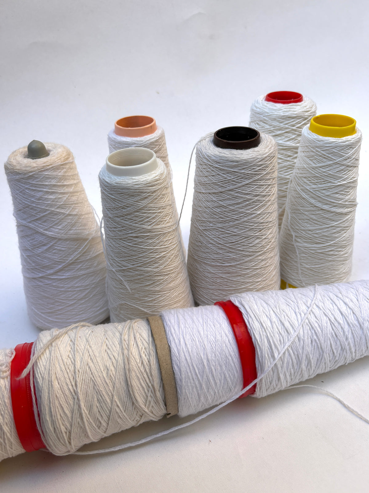 Assorted white yarn cones displayed in a grouped arrangement on white.