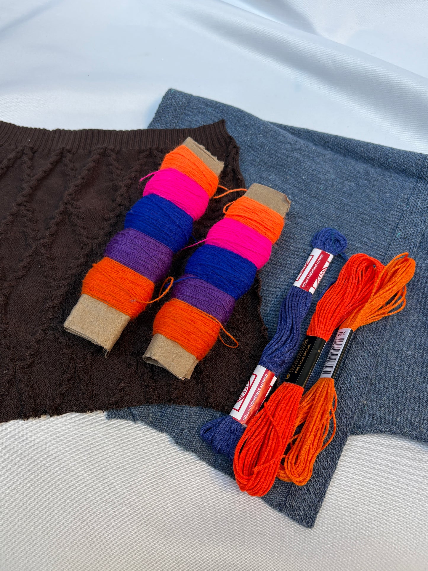 Mixed fabric swatches styled with bright thread spools and colourful embroidery floss.