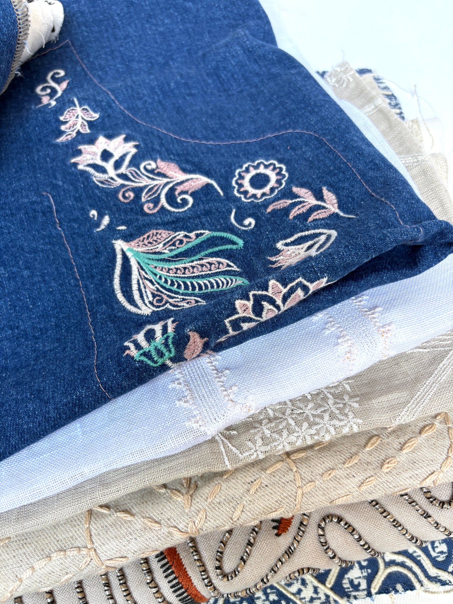 Stack of embroidered fabric samples with various patterns and colours.