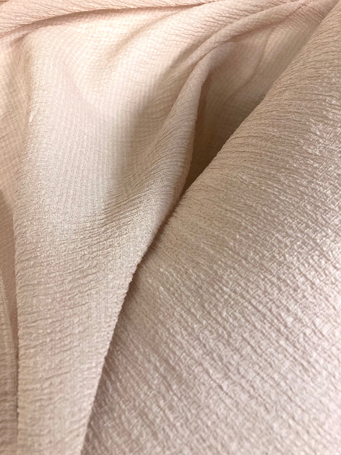 A close-up of wrinkled fabric in a peach colour, showing the texture