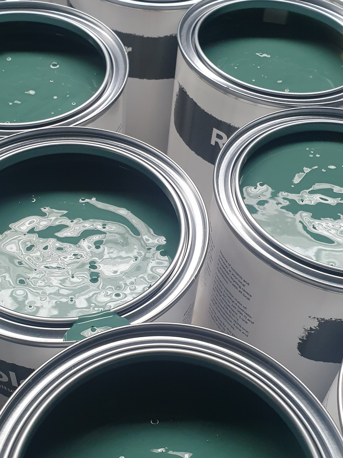 Close-up of multiple open cans of dark green paint.