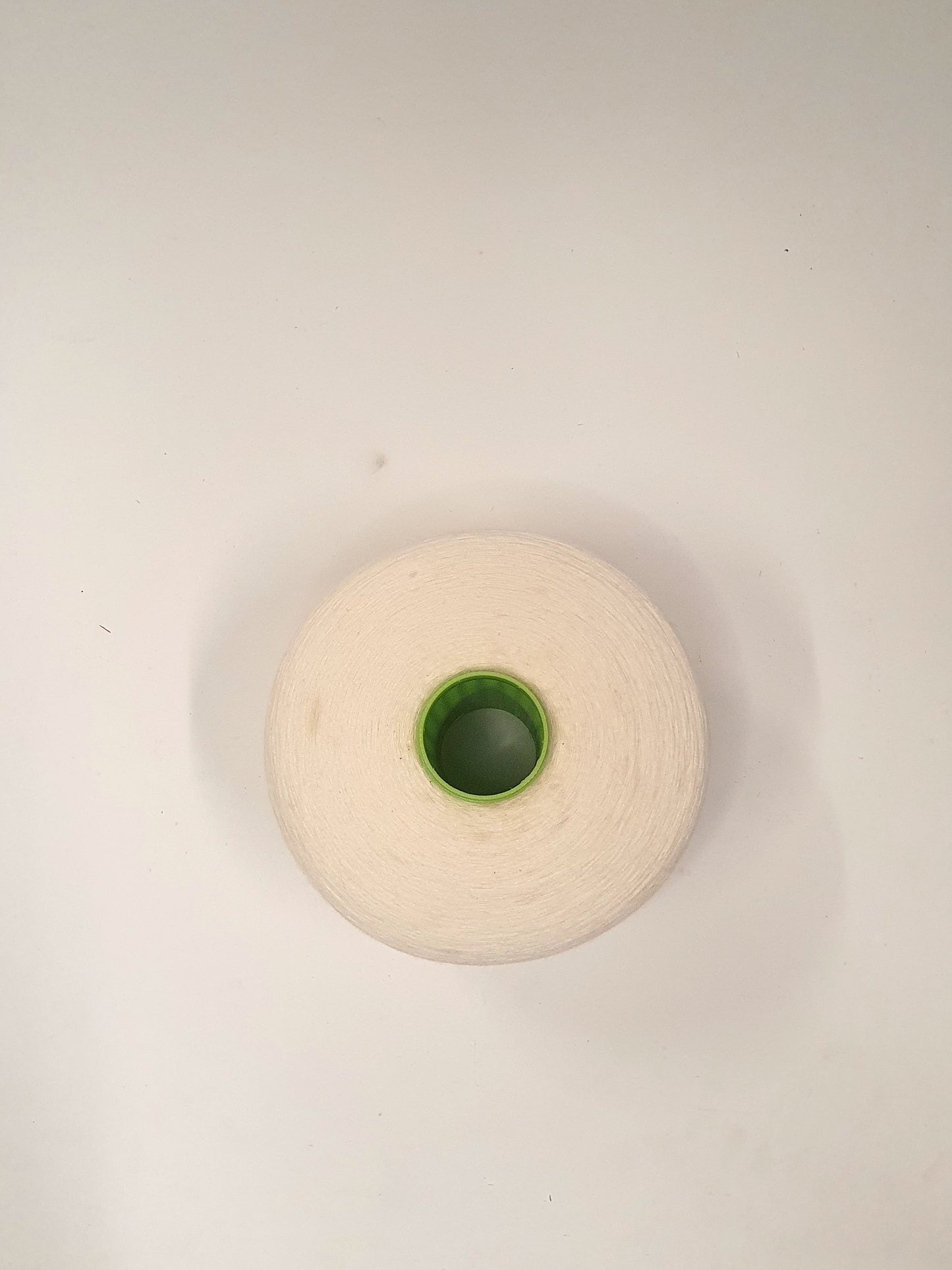 Close up of a single white yarn cone with a green cap, indicative of being used for knitting or crafting purposes from its top.