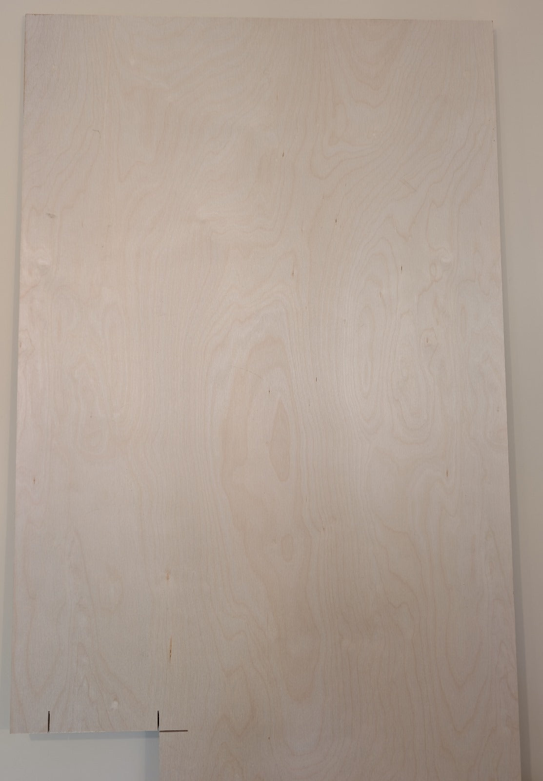 The top part of the birch plywood sheet with a visible grain pattern, with marks of previous use on the bottom left.