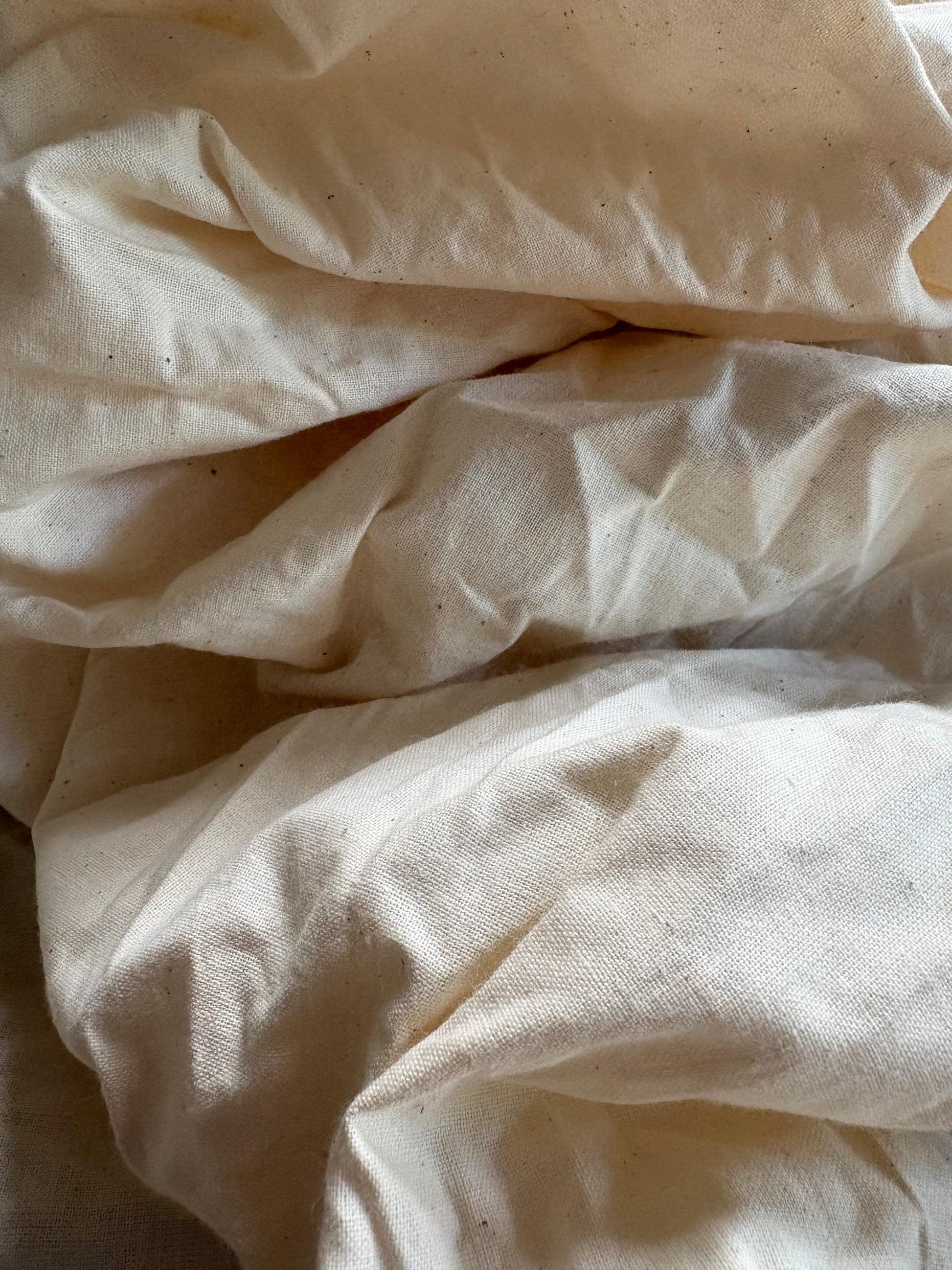 Off-white cotton calico fabric loosely arranged in soft creases.