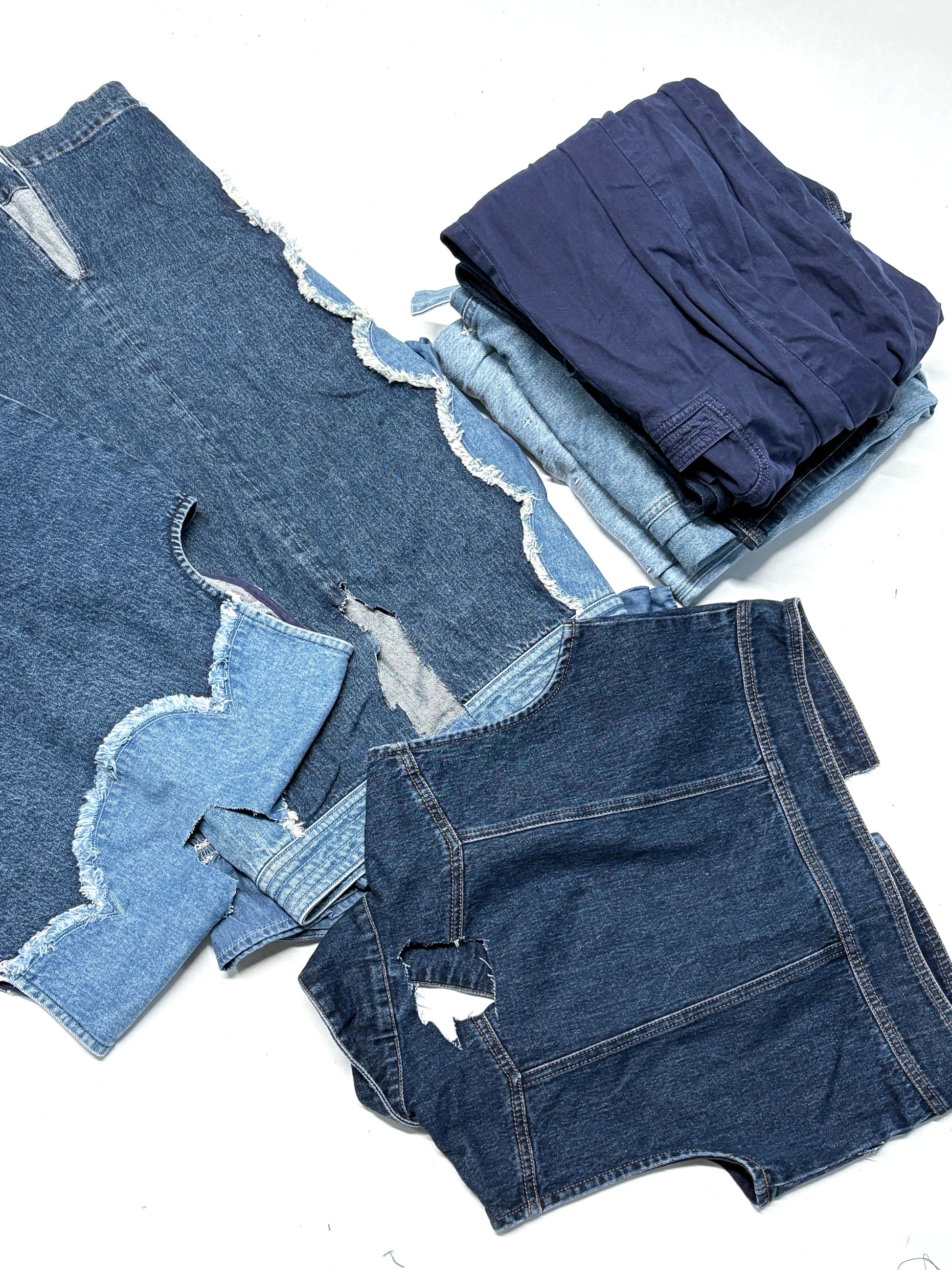 Stack of various denim items including shorts and pants on a white background
