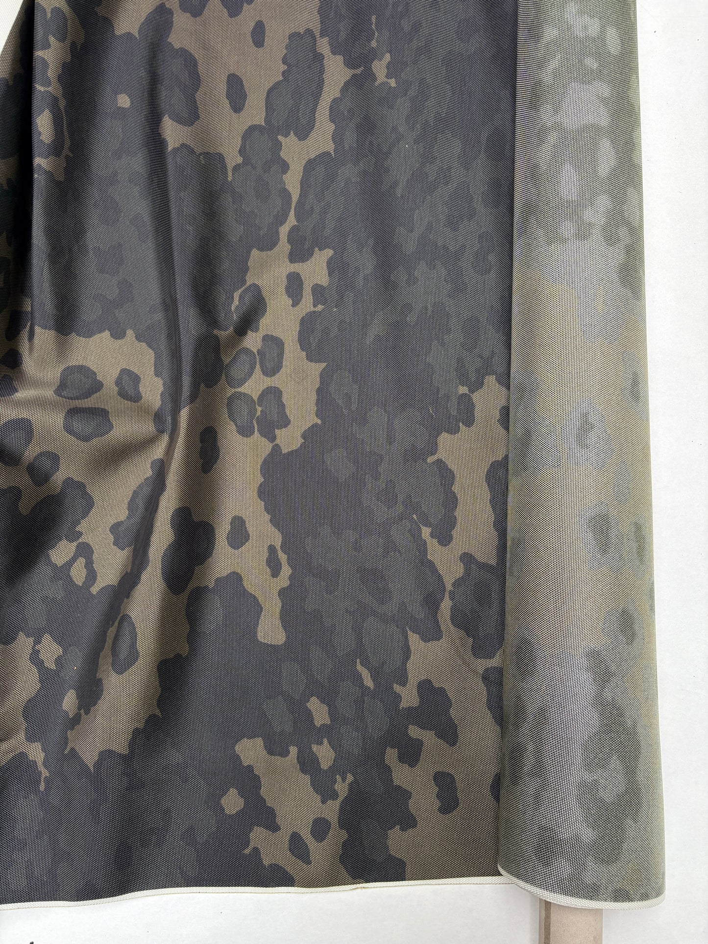 A folded fabric view highlighting the dark green-khaki camouflage pattern.