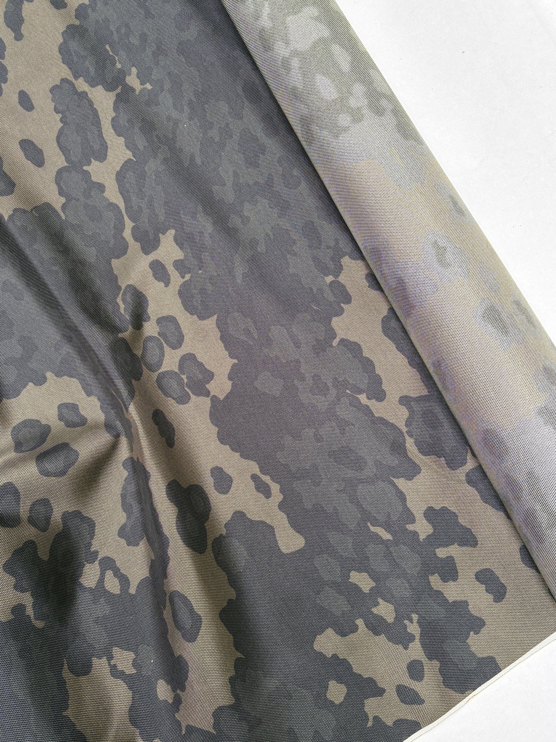 Camouflage fabric in dark green and khaki with soft folded texture.