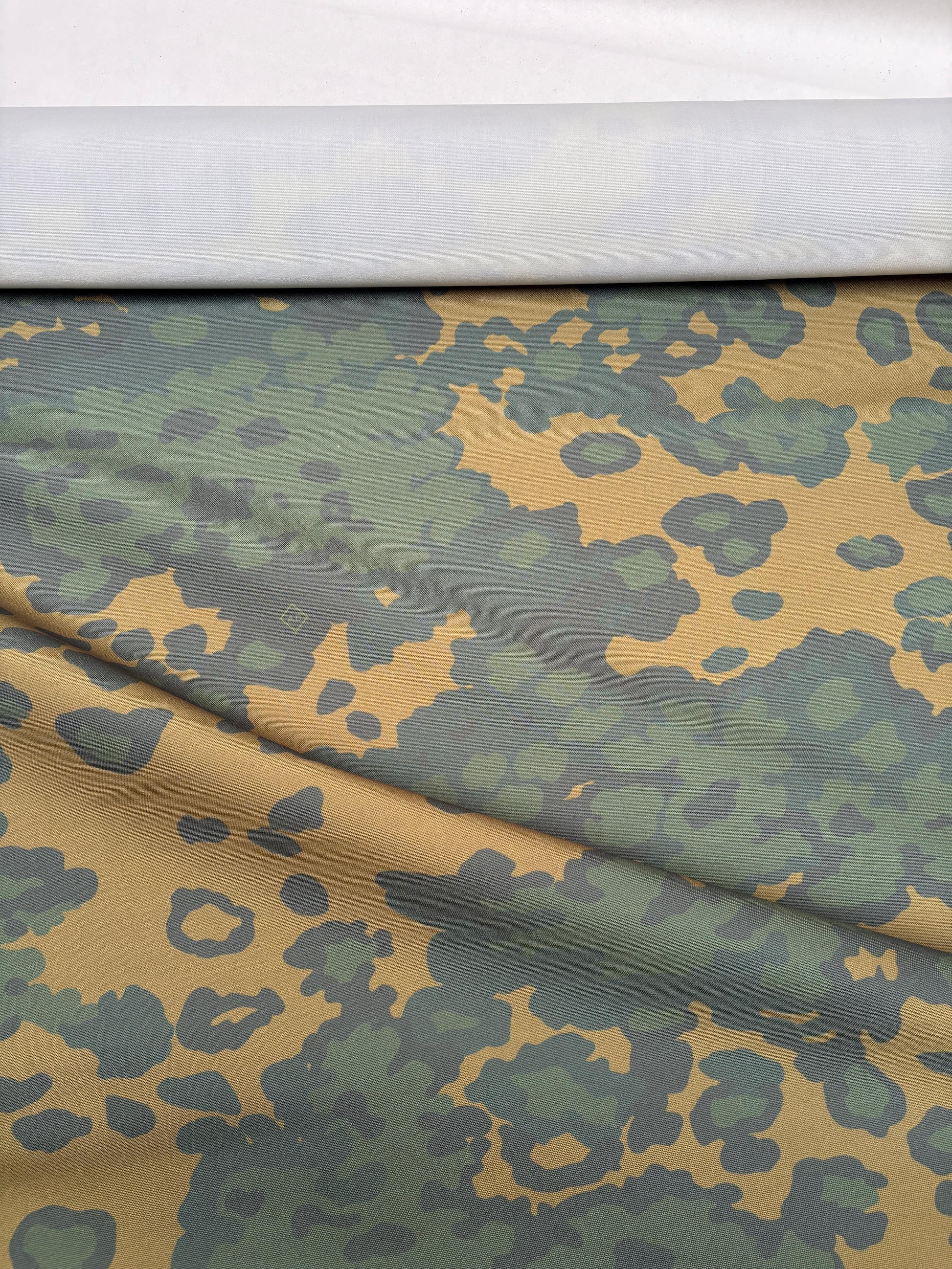Green and brown camouflage fabric laid flat to show the pattern.