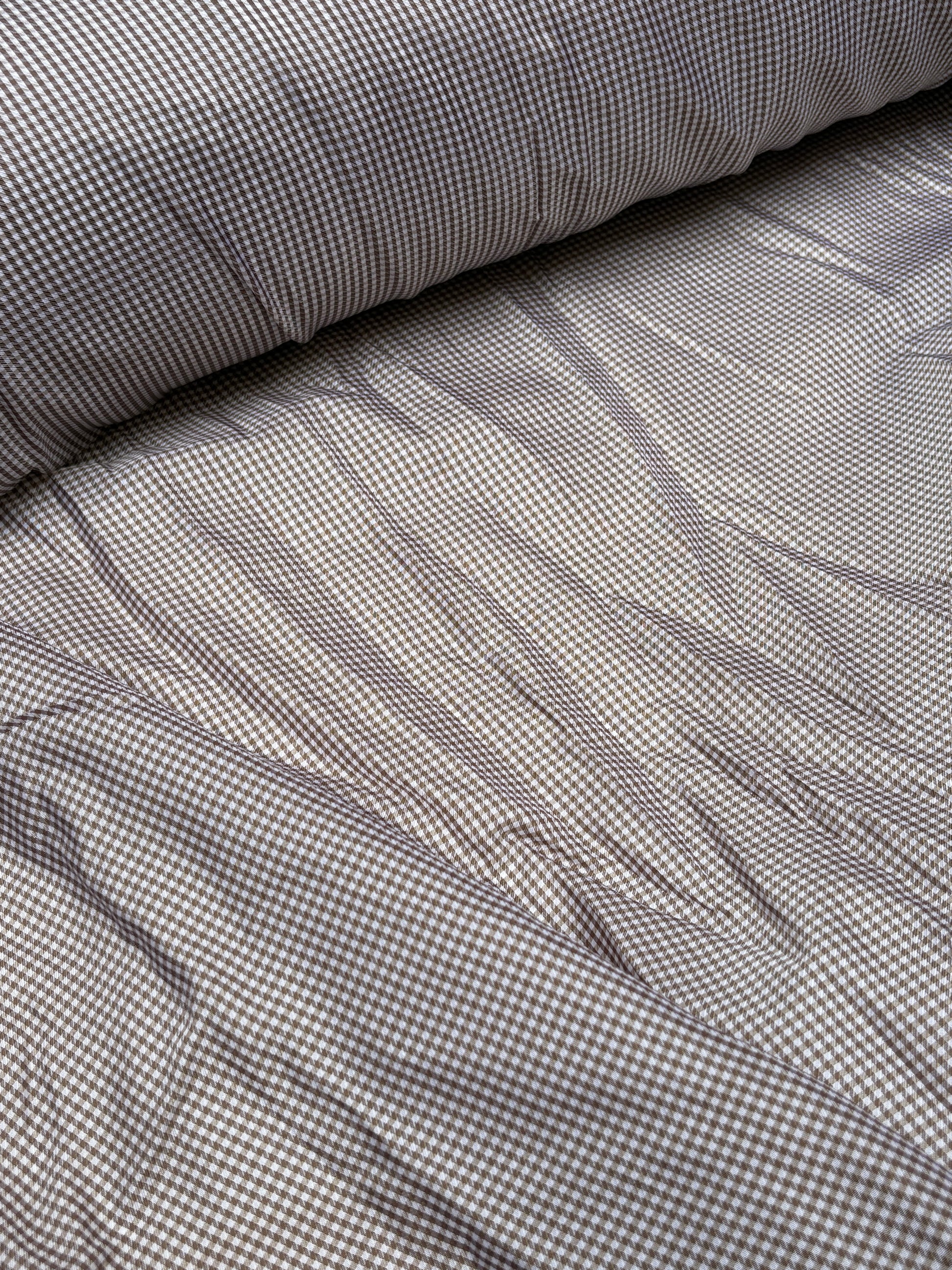 Checked fabric is unrolled and spread across a white surface