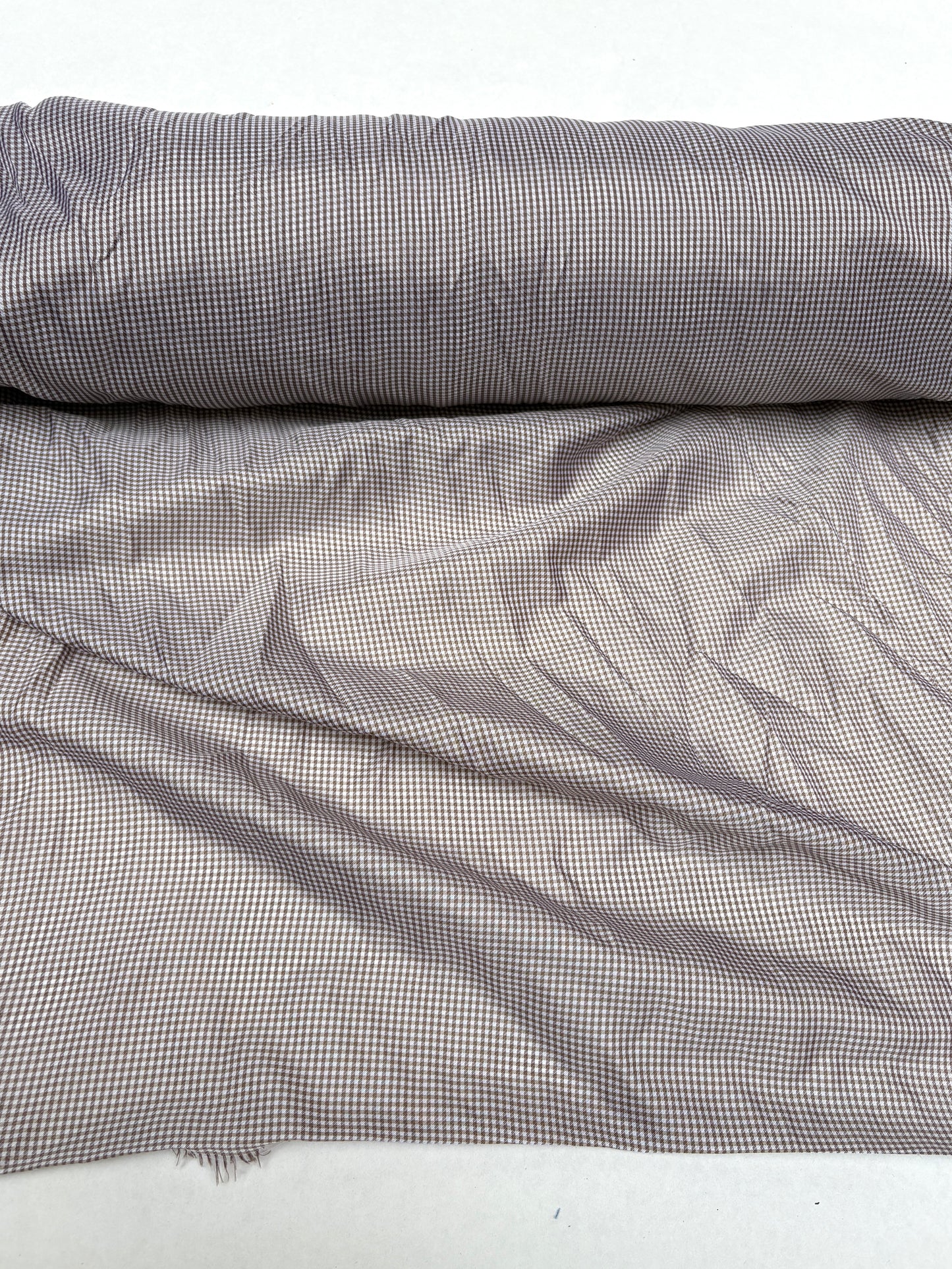Fine patterned fabric is shown hanging from a rolled edge on white background