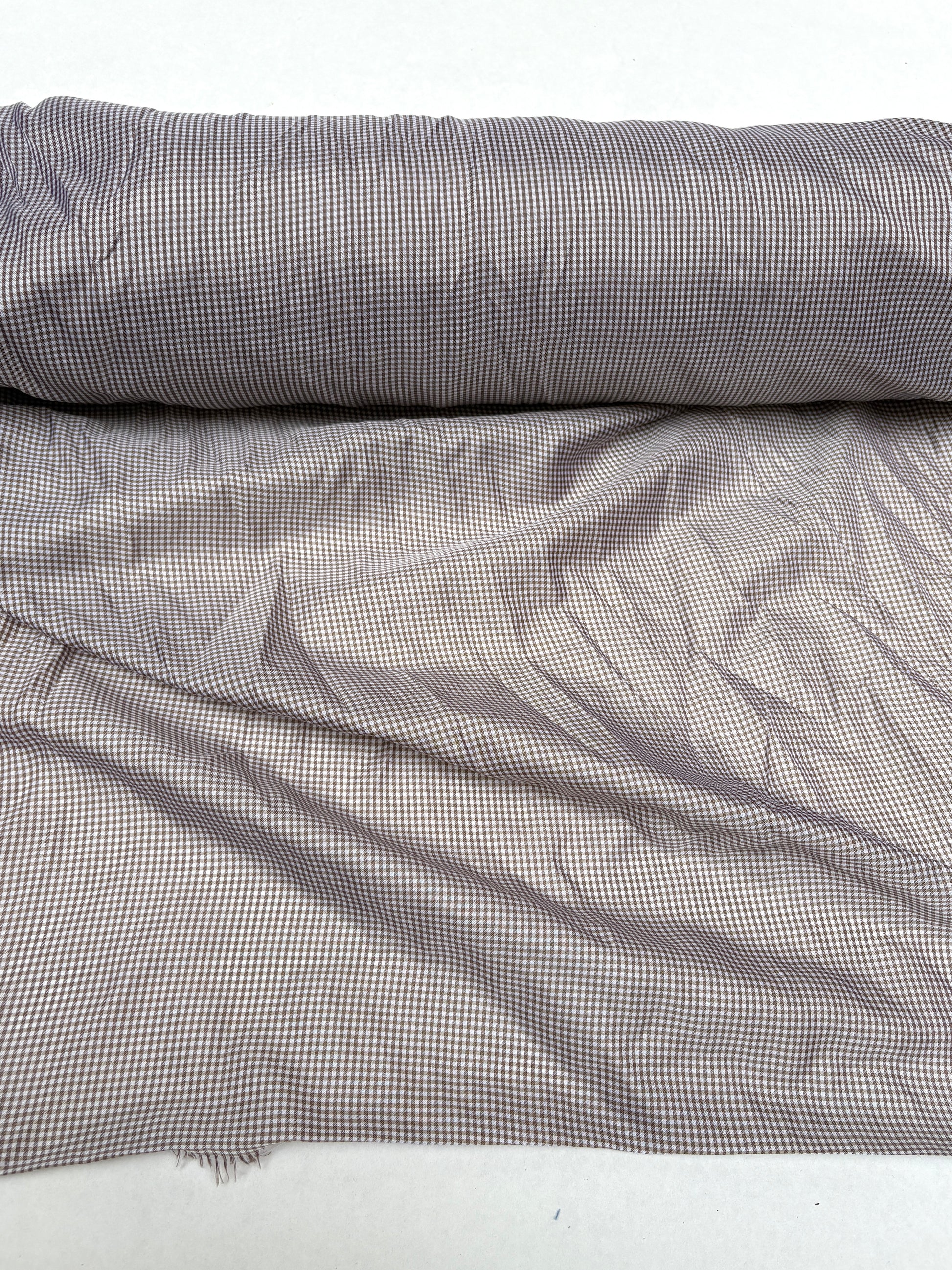 Fine patterned fabric is shown hanging from a rolled edge on white background