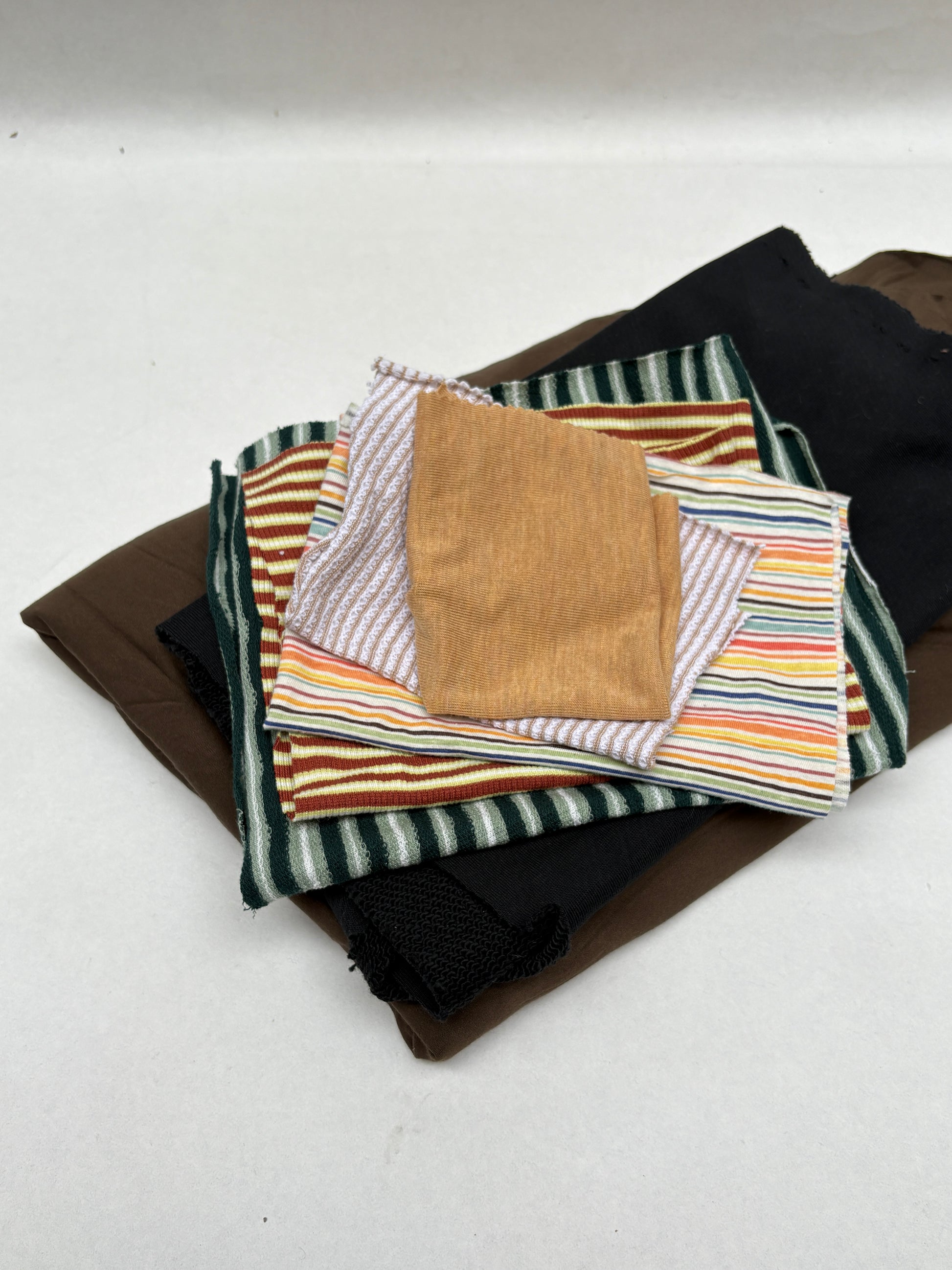 Layered mixed fabric pieces with striped and plain swatches on white.