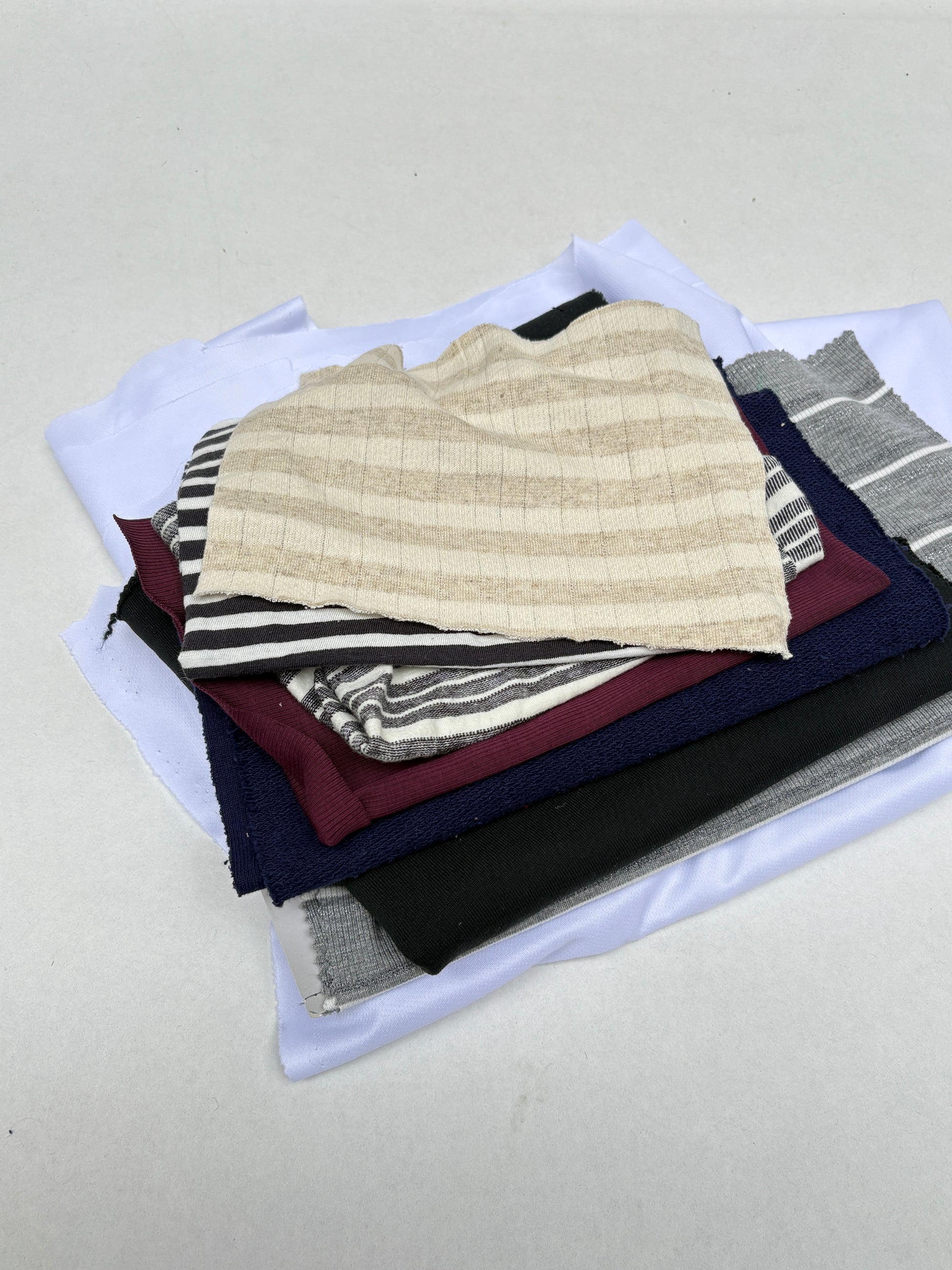 Stacked mixed fabric pieces with striped and plain textures on white.