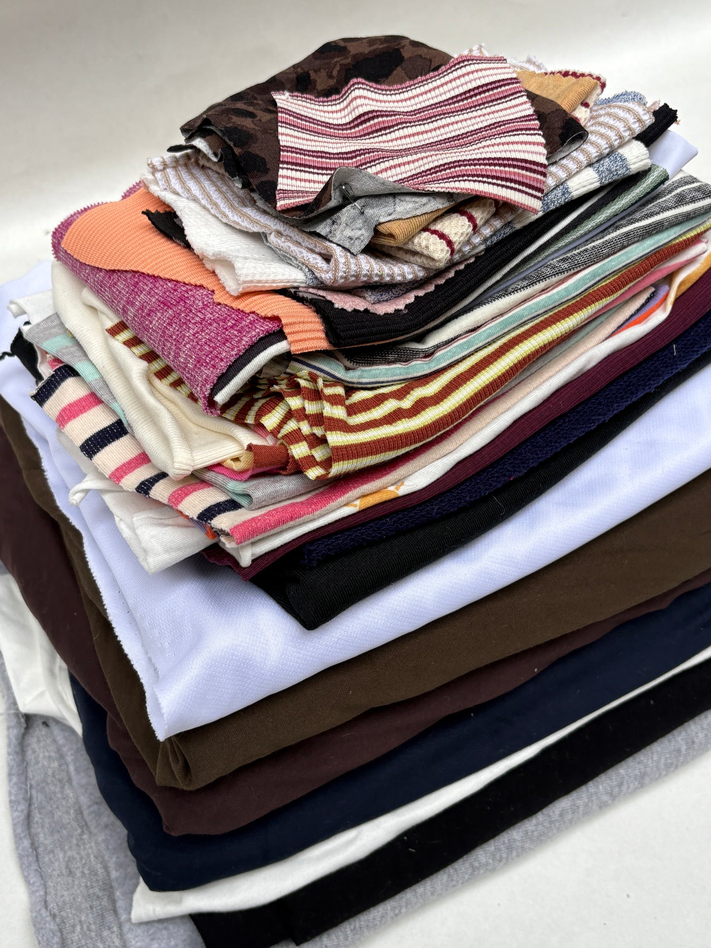 Stacked mixed fabric pieces with assorted patterned swatches on a white background.
