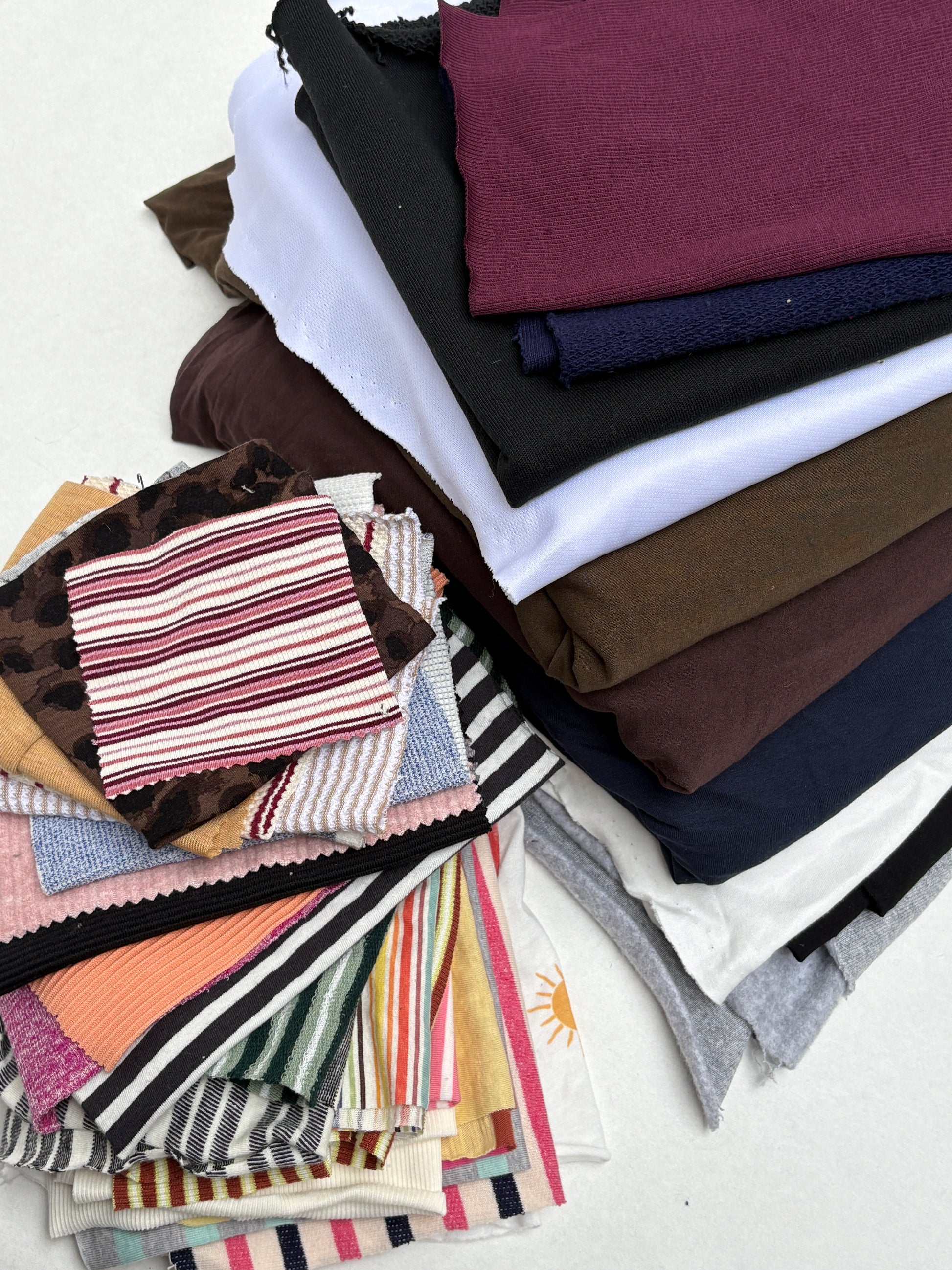 Mixed fabric pieces and patterned swatches layered in assorted colours on white.