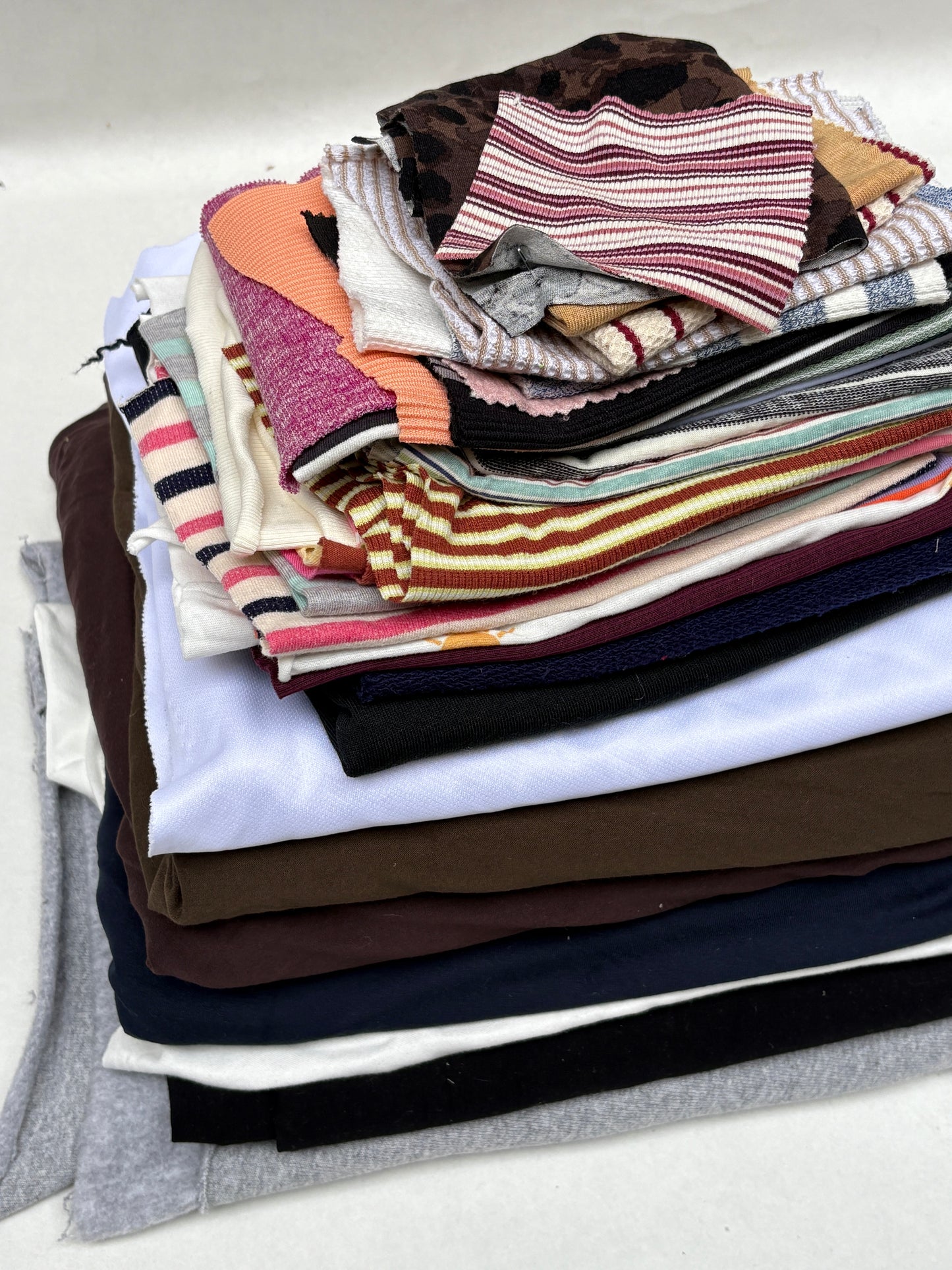 Stacked mixed fabric pieces with assorted striped and patterned swatches on white.