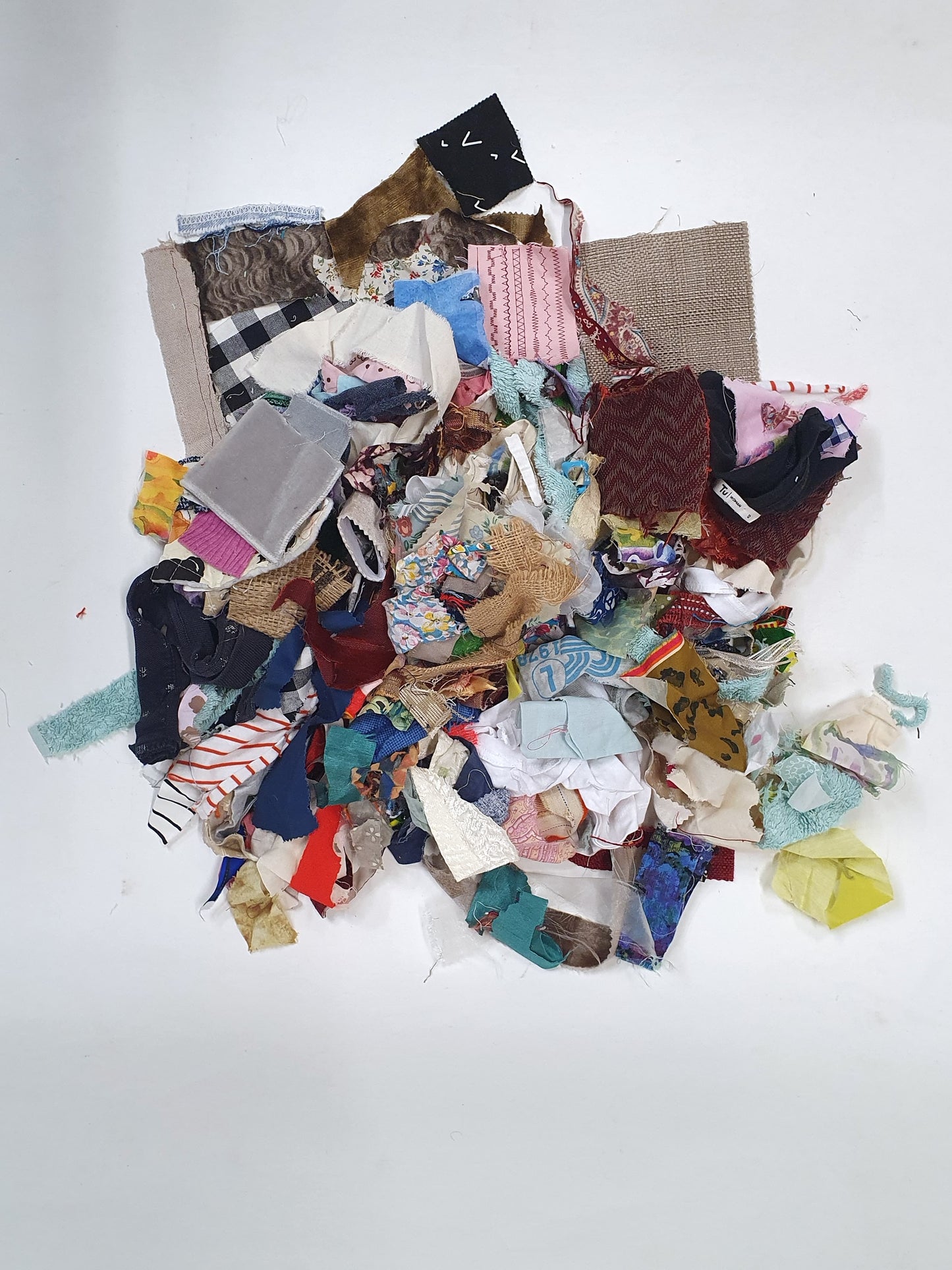 Pile of mixed fabric offcuts in assorted colours, prints, patterns and textures on white.