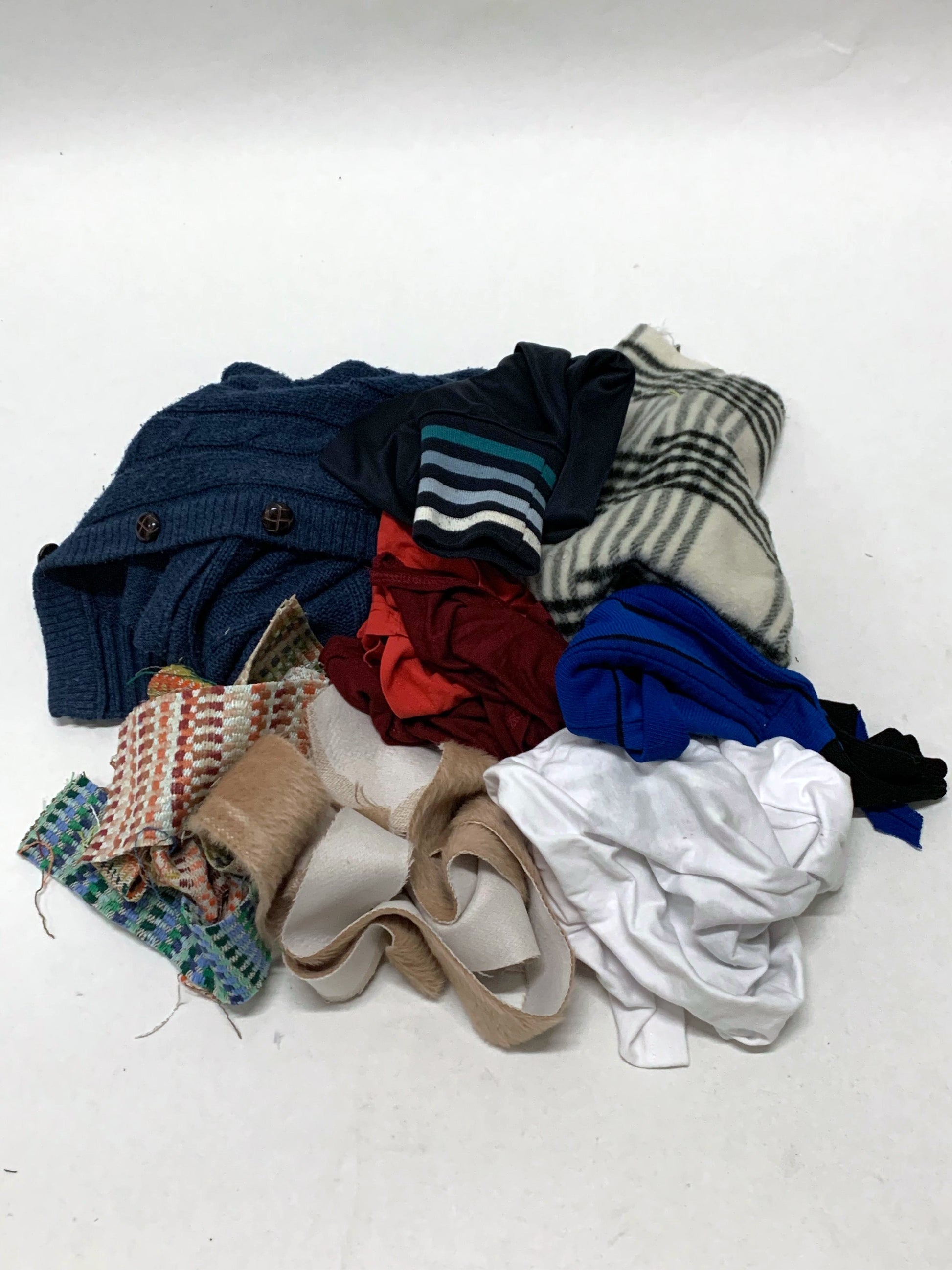 Pile of mixed fabric offcuts in assorted colours, textures and patterns on white.