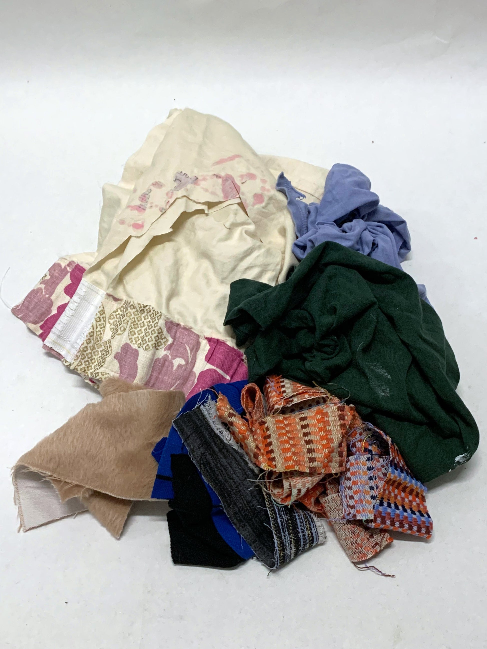 Pile of mixed fabric offcuts in assorted colours, prints and textures on white.