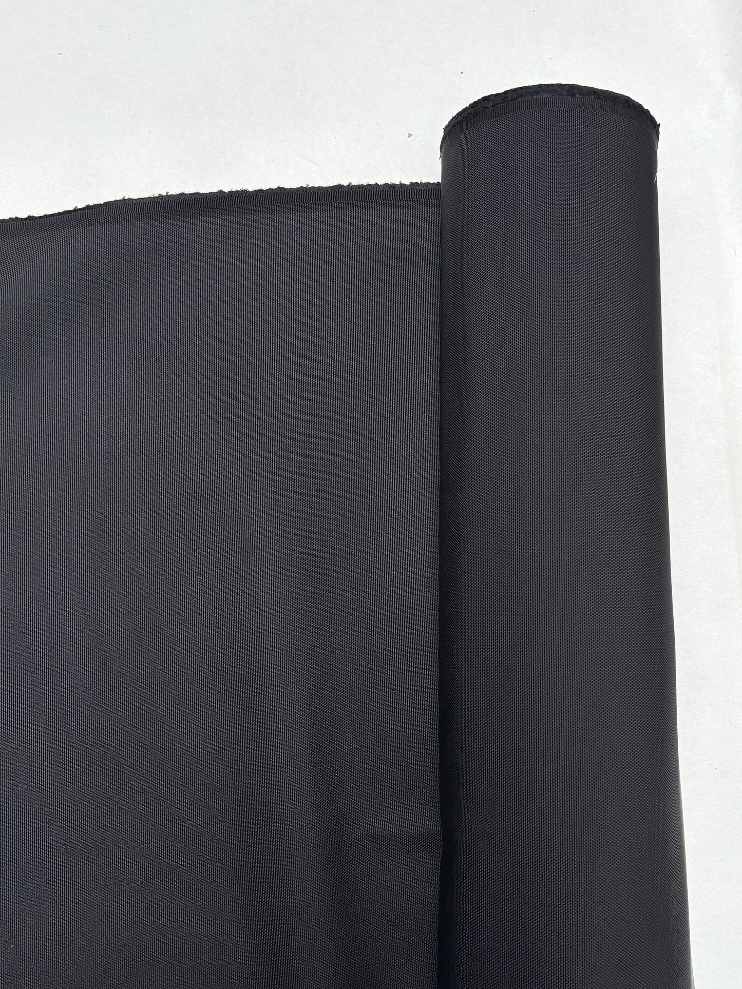 Dark textured fabric is shown hanging from a roll