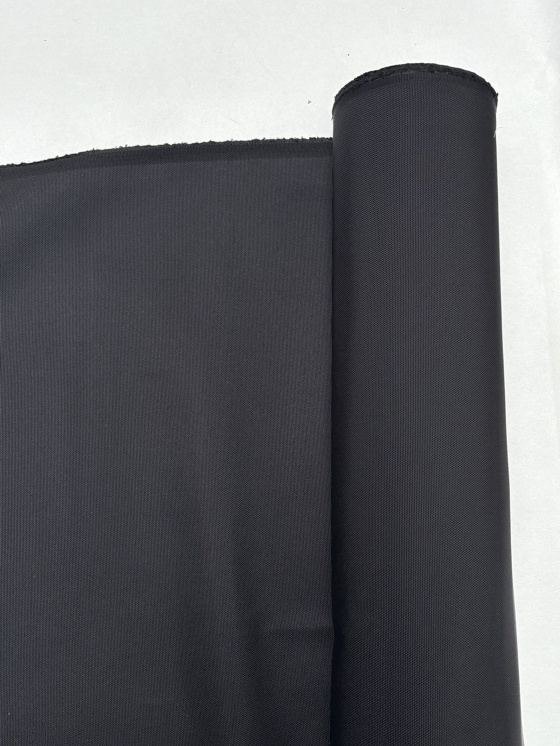 Dark textured fabric is shown hanging from a roll