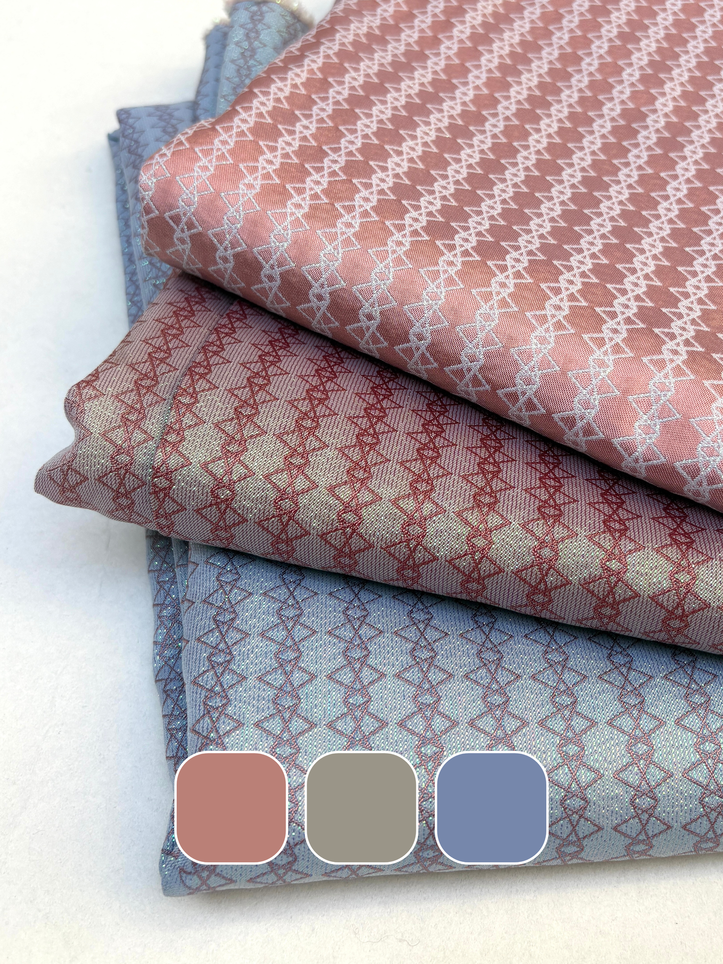 Stack of patterned silk fabric in pink, gray, and blue folded on a white background.