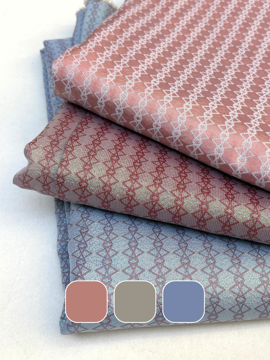 Stack of patterned silk fabric in pink, gray, and blue folded on a white background.