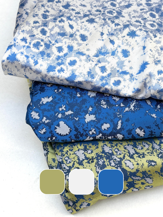 Stack of folded silk fabric with blue, white, and yellow floral patterns on a white background.