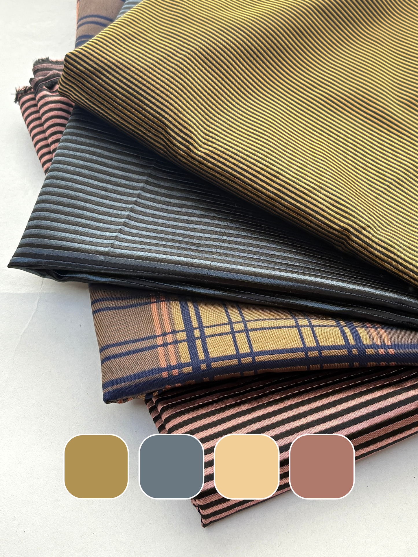 Stack of silk fabric in brown, gray, and plaid patterns with colour swatches below.
