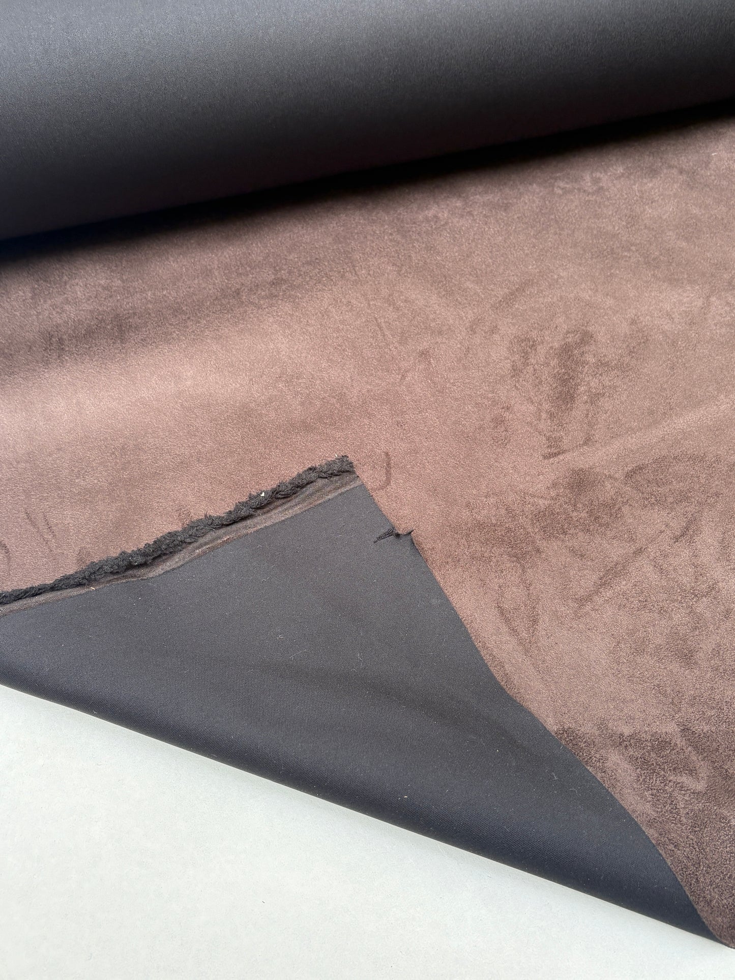 Brown suede-textured fabric hangs beneath a rolled fabric edge