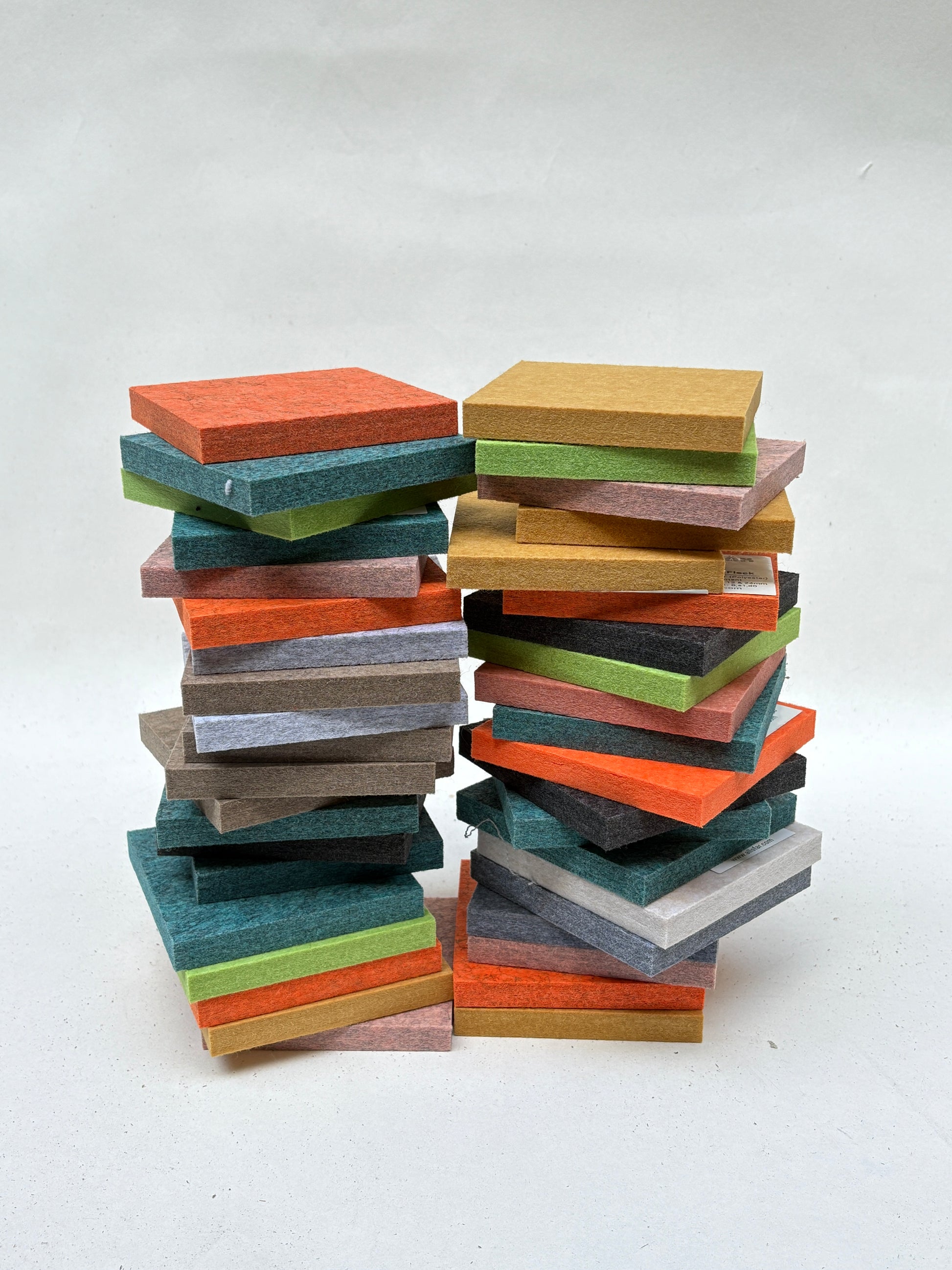 Mixed felt tiles are stacked in colourful piles on a white background