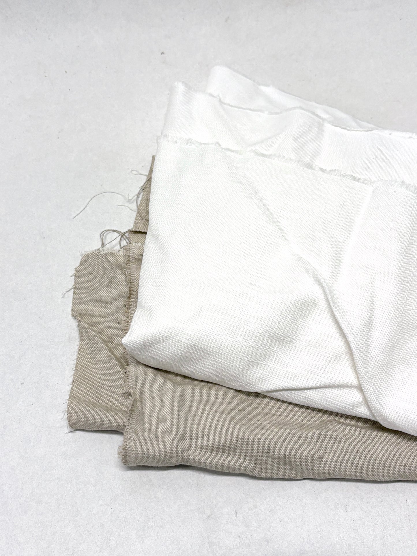 Two folded fabrics, one white and one beige, on a light gray background