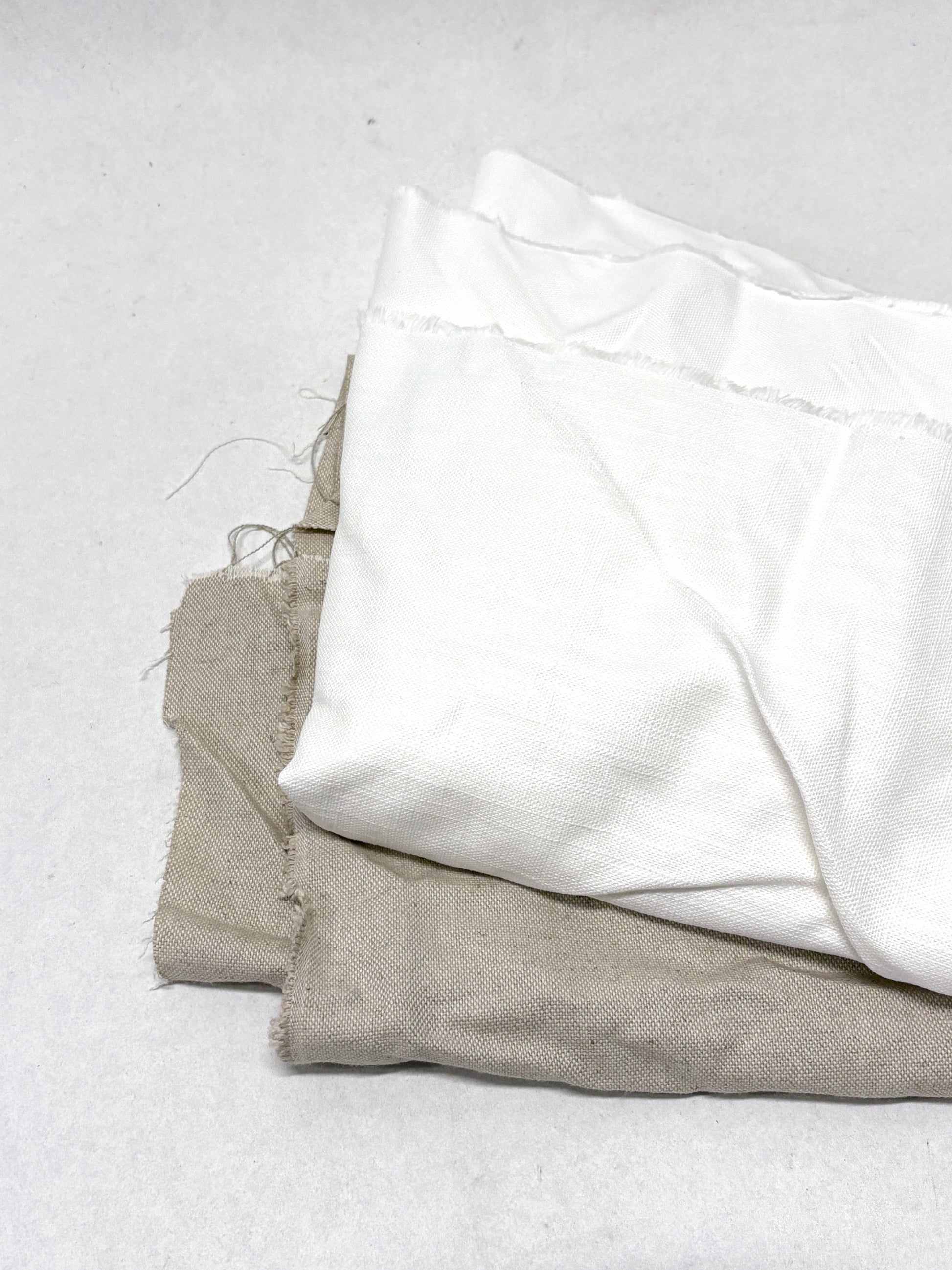 Two folded fabrics, one white and one beige, on a light gray background