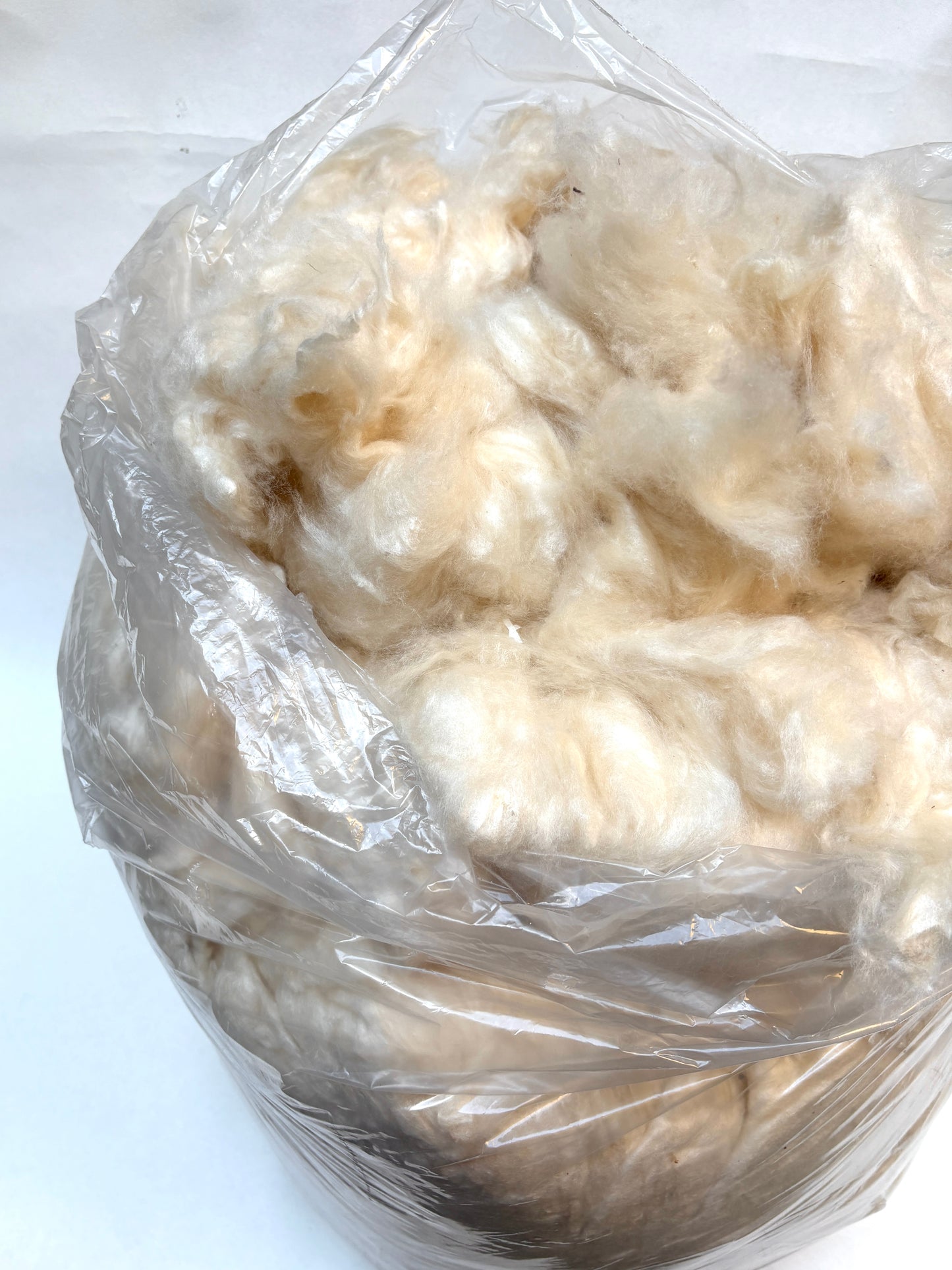 Ball of white wool stuffing wrapped in clear plastic on a white background