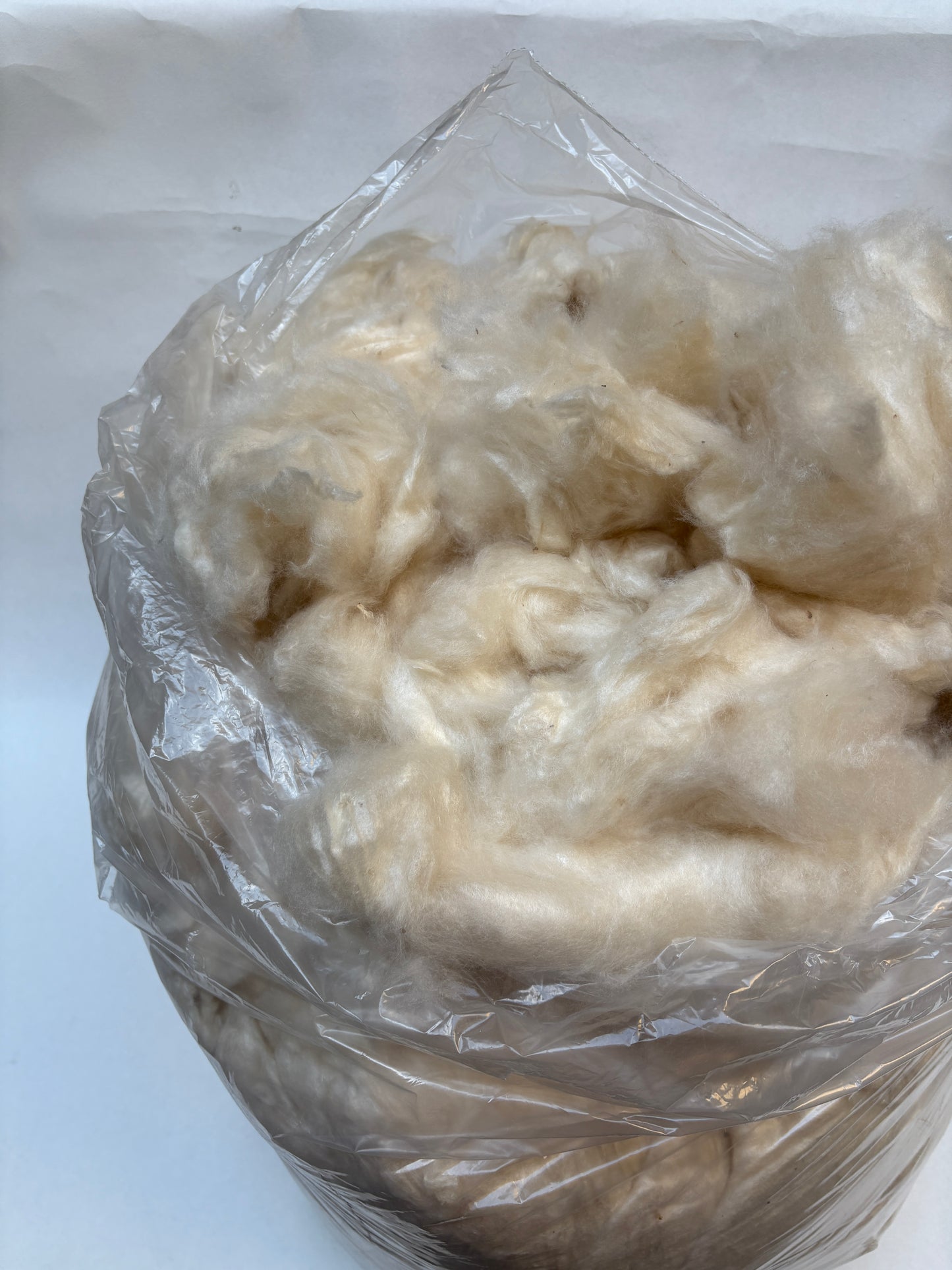 A bag filled with soft off-white raw fibre material.