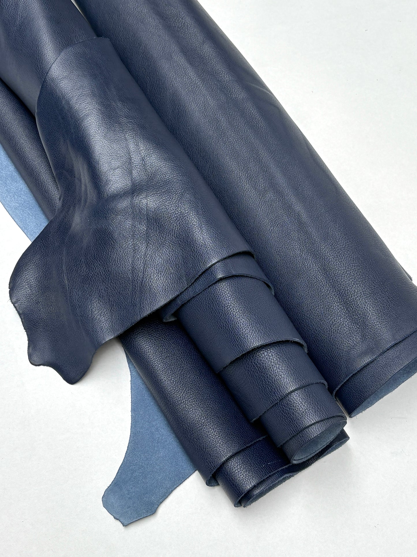 Rolled blue leather hides are stacked on a white background