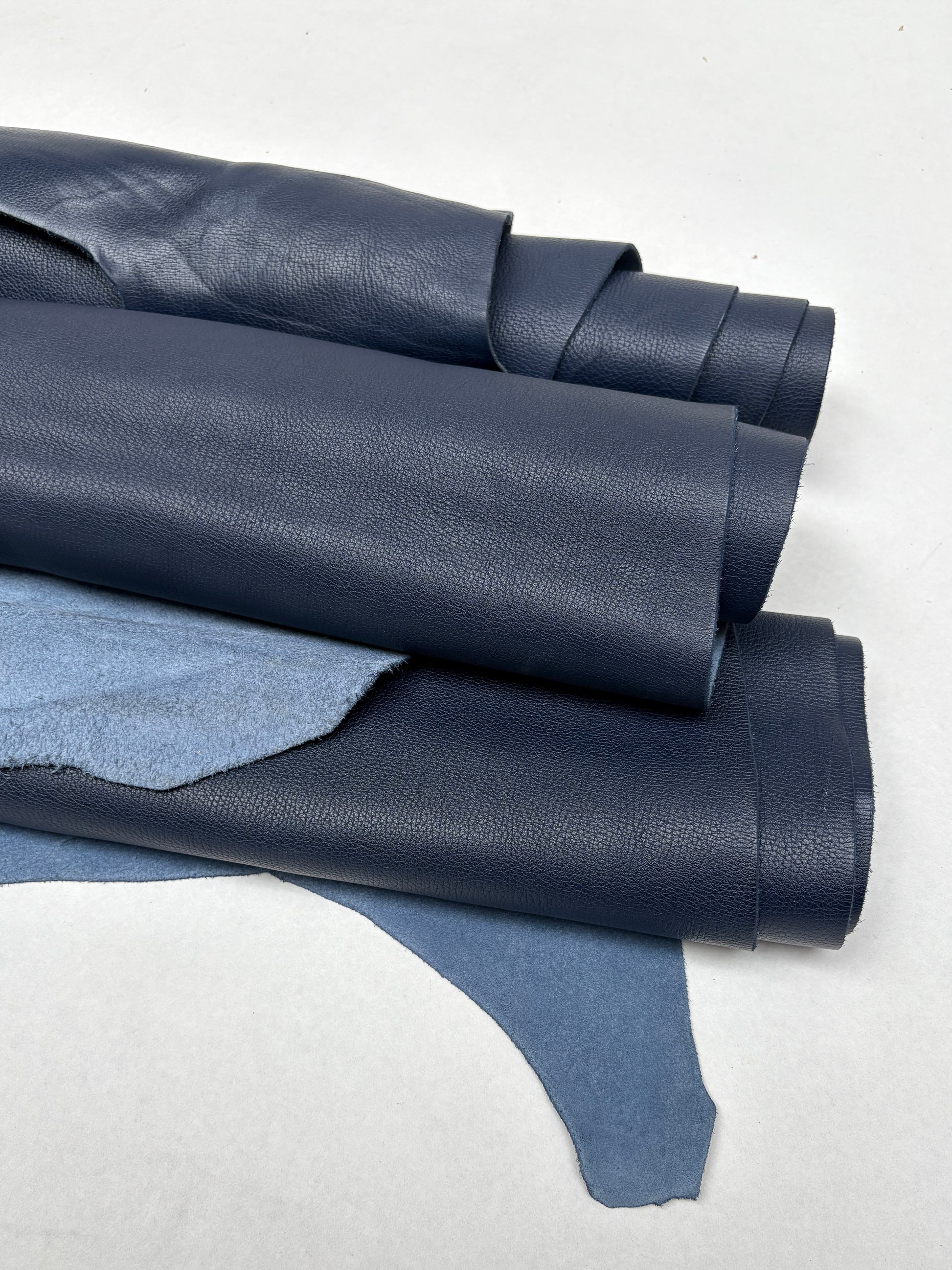 Blue leather hides are arranged in overlapping rolled layers