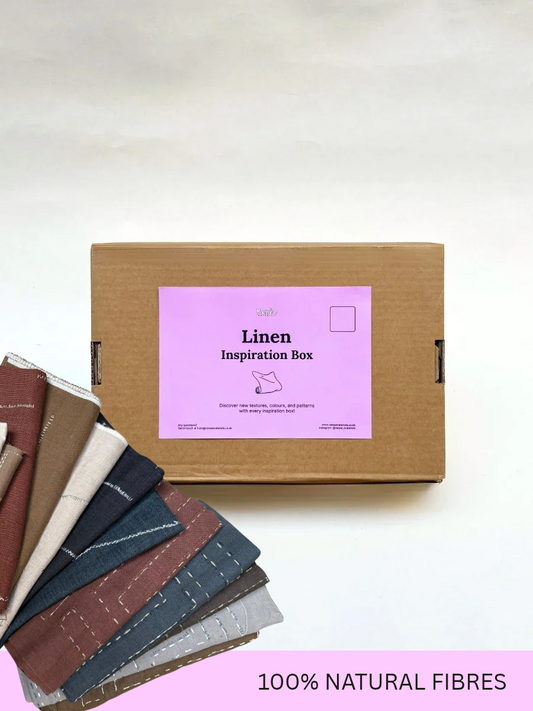A brown cardboard box labeled 'Linen Inspiration Box' sits on a light background, with several linen fabric swatches fanned out in the lower left. A pink banner at the bottom reads '100% NATURAL FIBRES'.