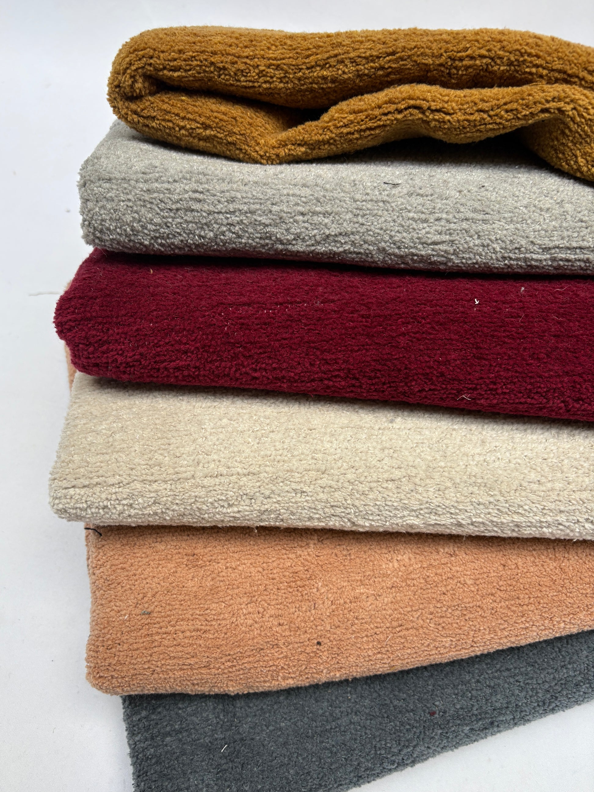 Textured fabrics in mustard, grey, red, cream, and peach are layered together