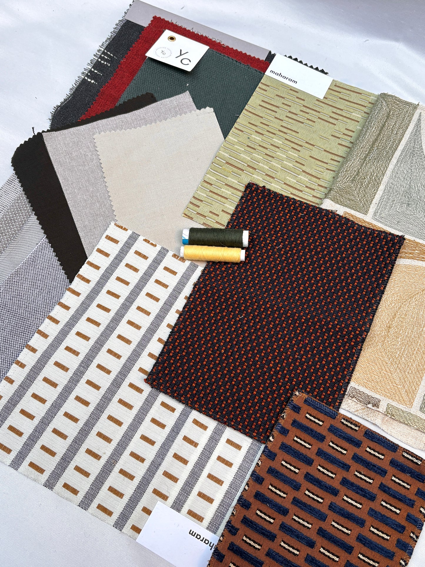 Assorted upholstery fabric swatches with varied patterns, textures and matching thread spools.