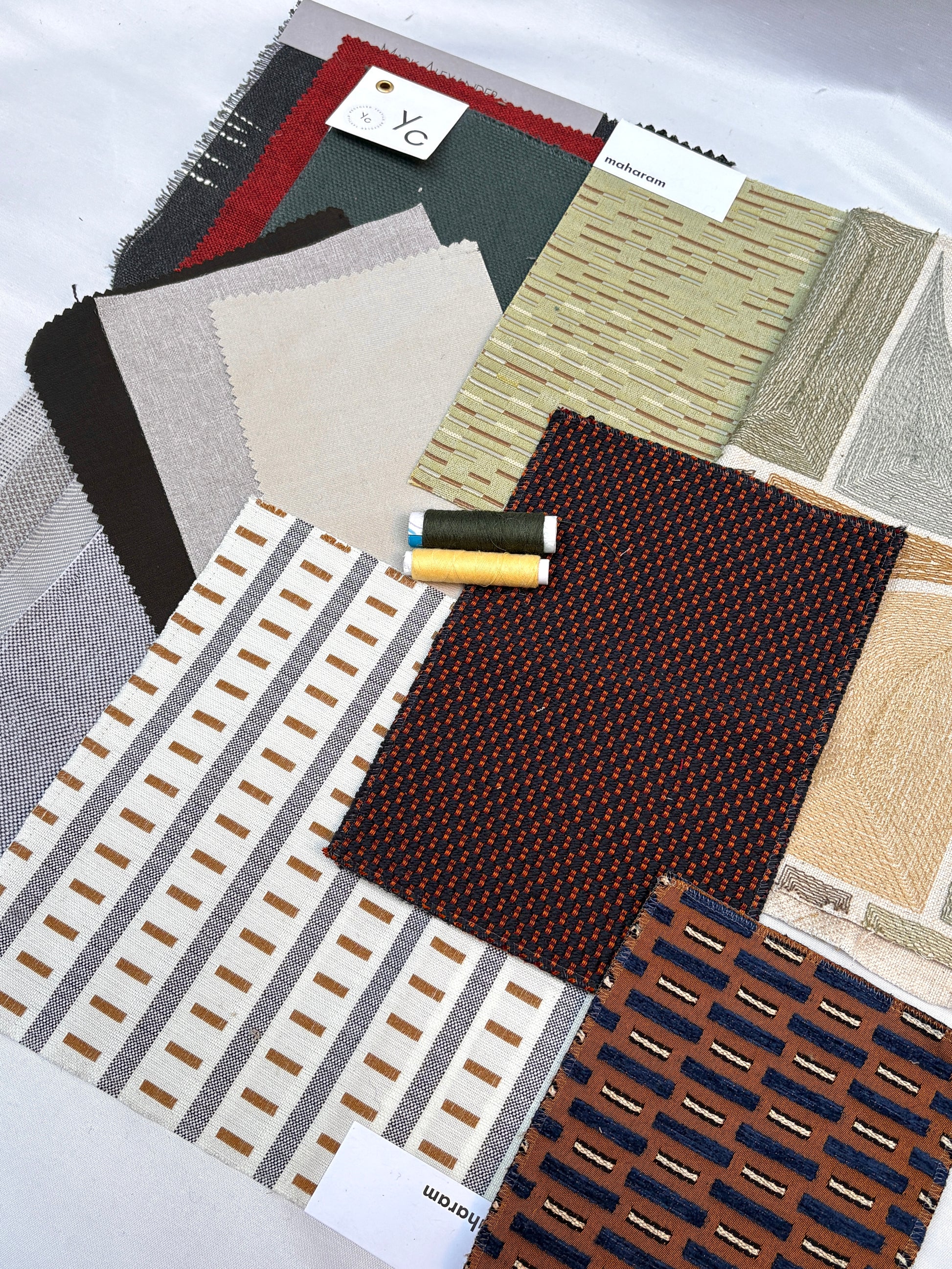 Assorted upholstery fabric swatches with varied patterns, textures and matching thread spools.