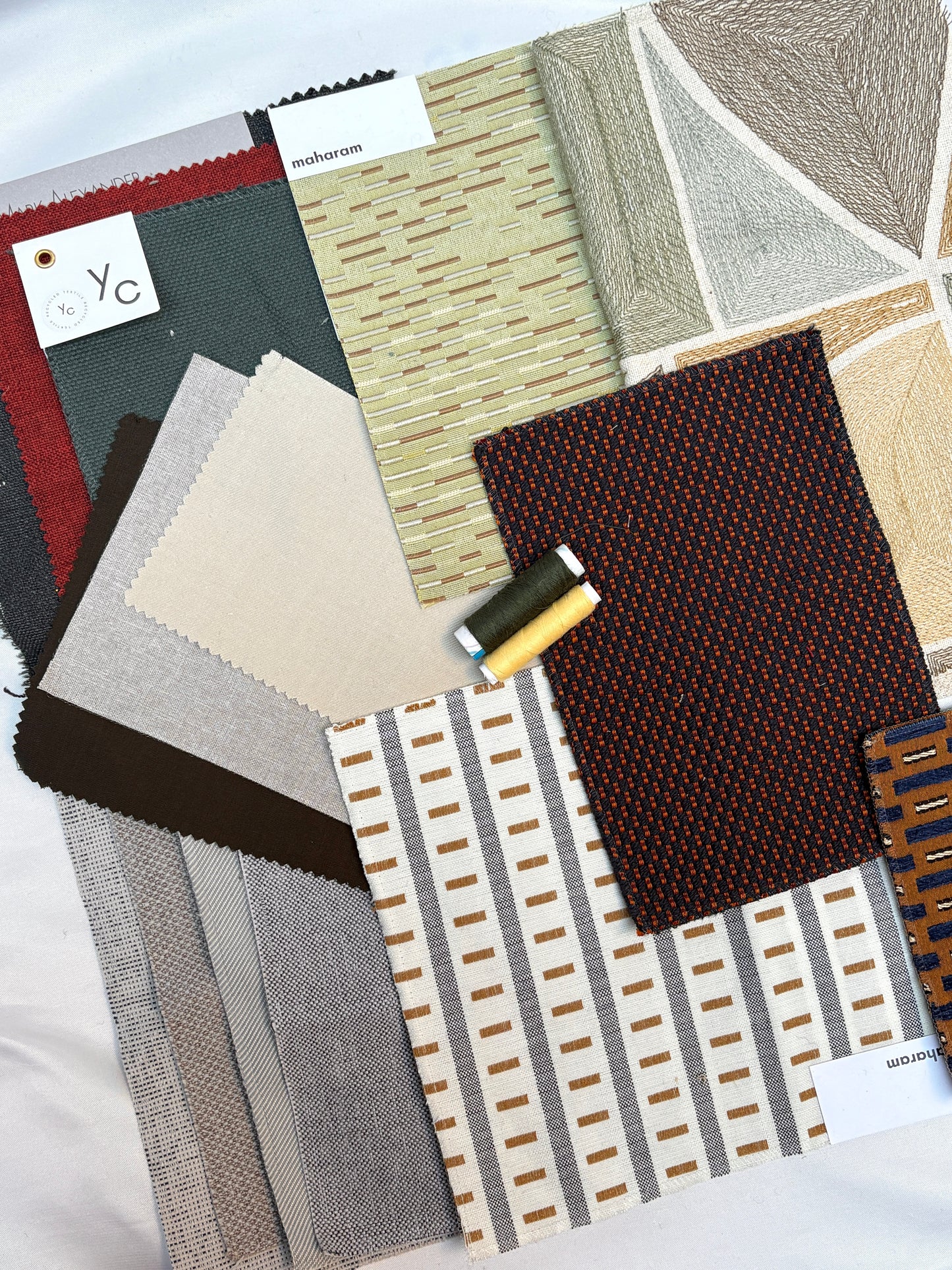 Mixed upholstery fabric samples with coordinating thread spools in warm neutral tones.
