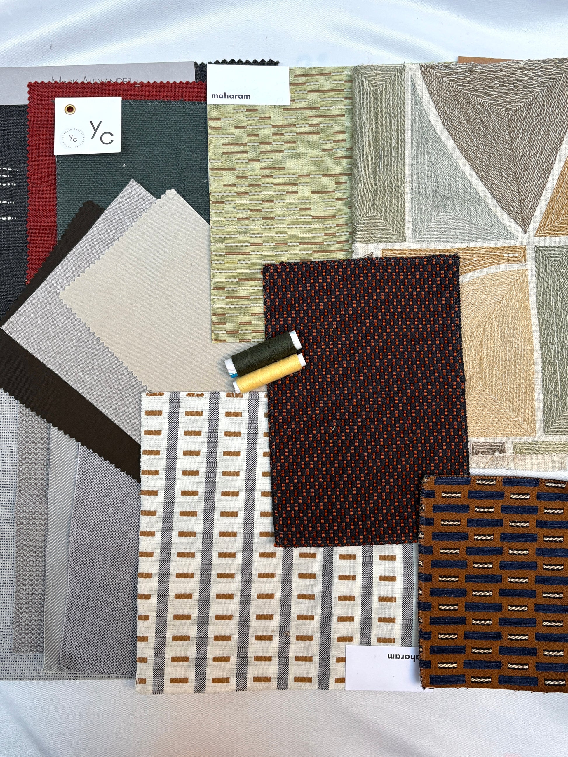 Layered upholstery fabric swatches with geometric patterns and matching thread spools.