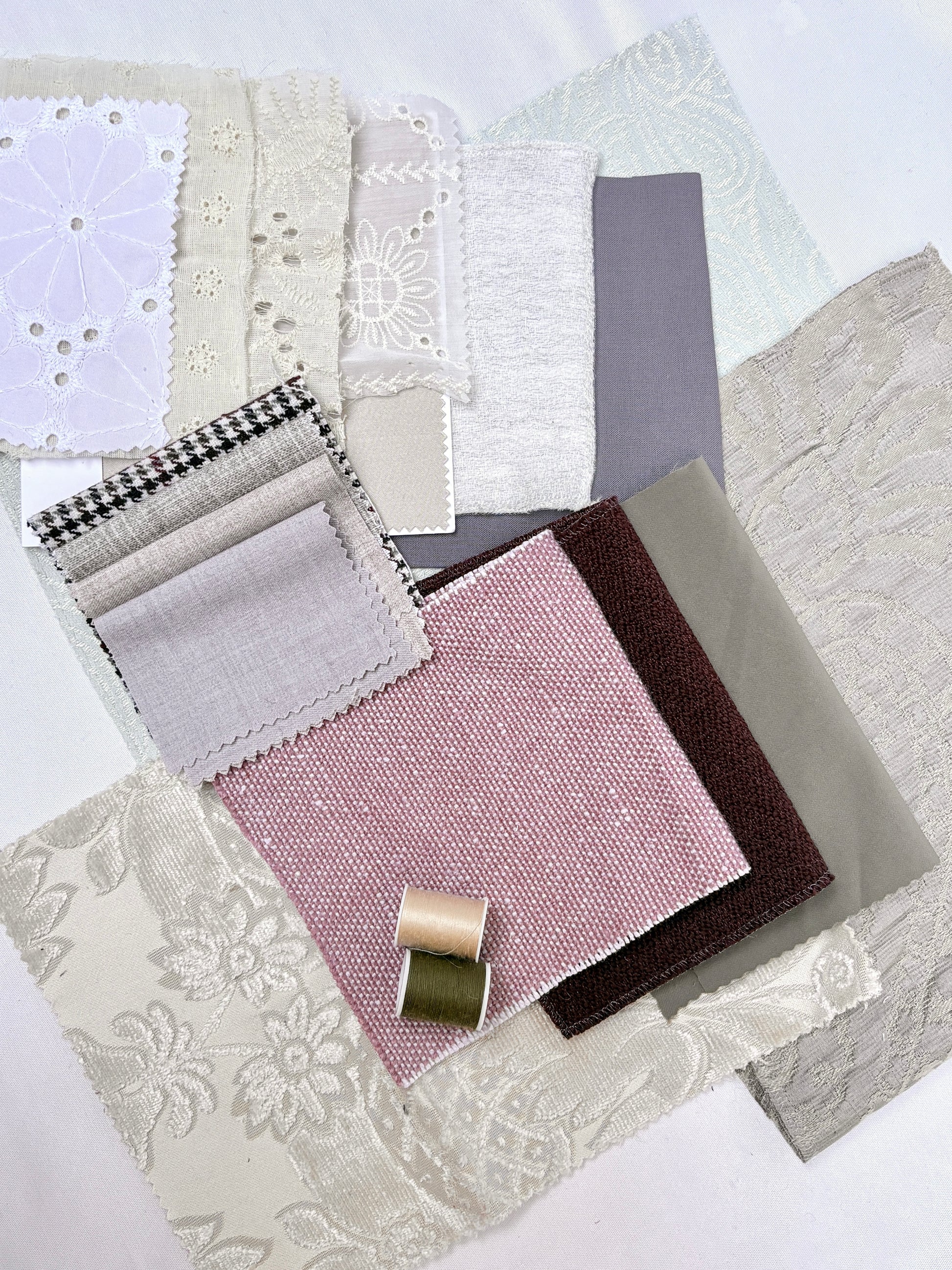 Layered fabric swatches in soft neutral tones with lace and thread spools.